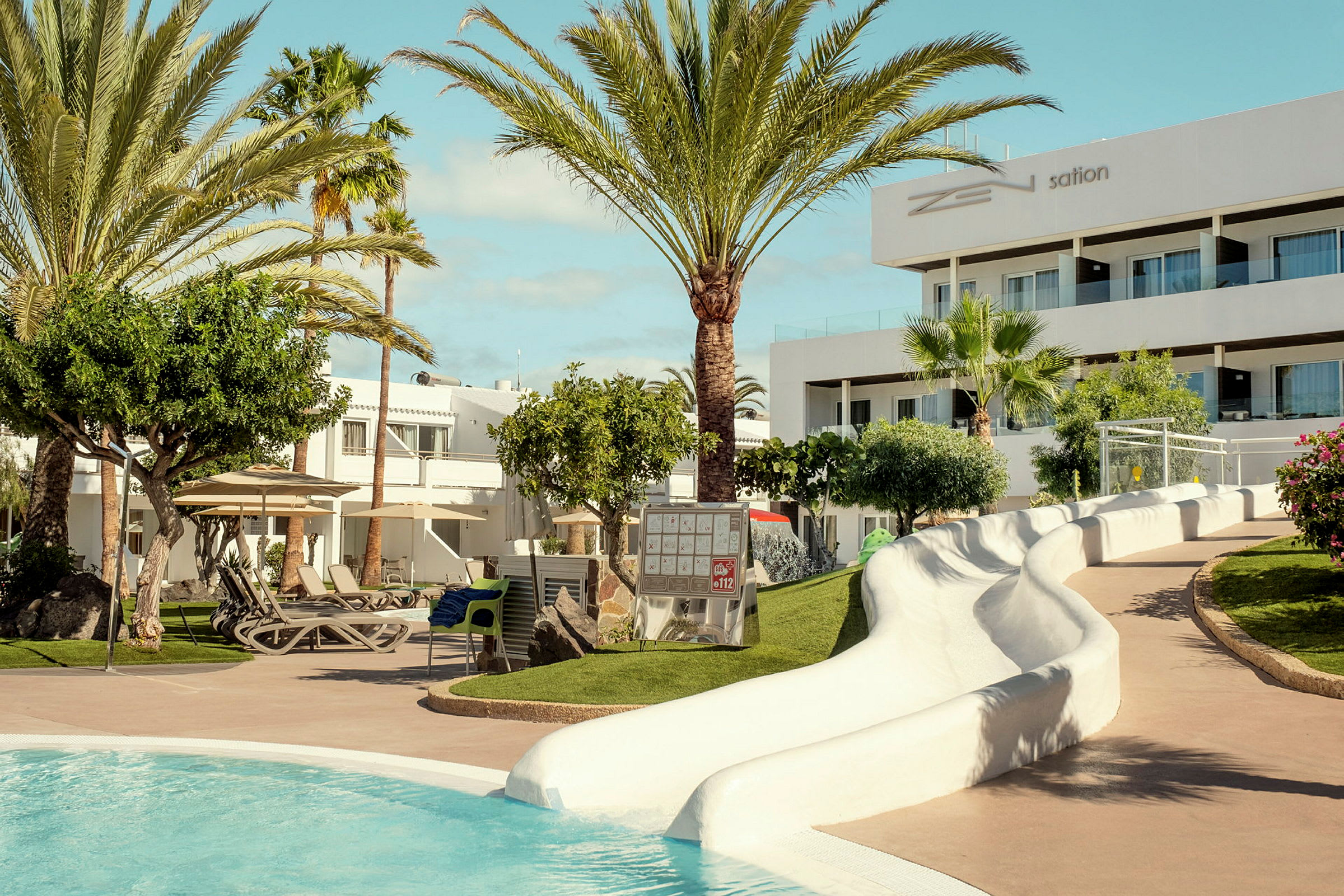Hotellets poolområde med gröna omgivningar, solsängar och en vattenrutschkana. (AI-genererad text)