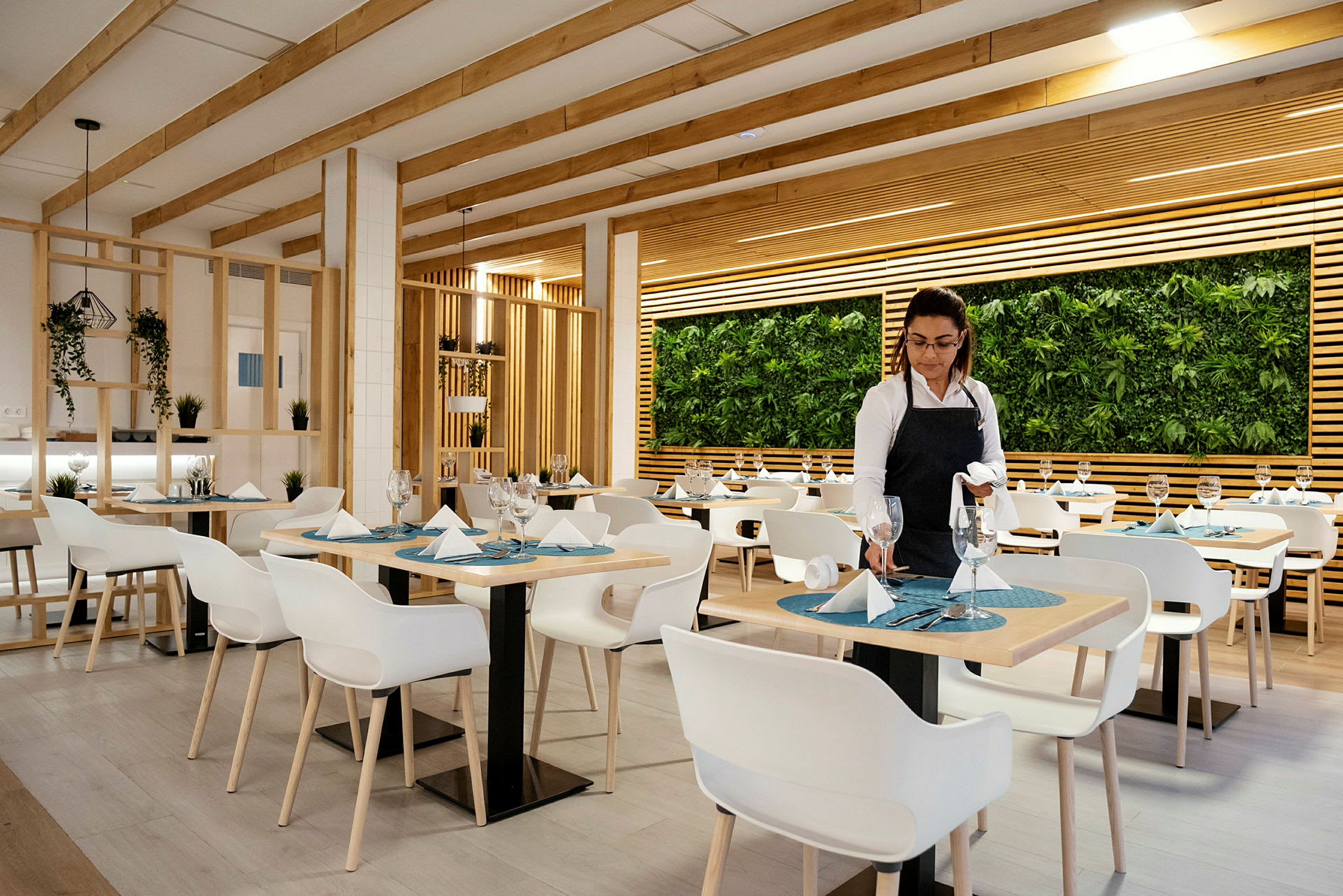 En restaurang med modern inredning med vita stolar, dukade bord och en vägg dekorerad med växter. (AI-genererad text)