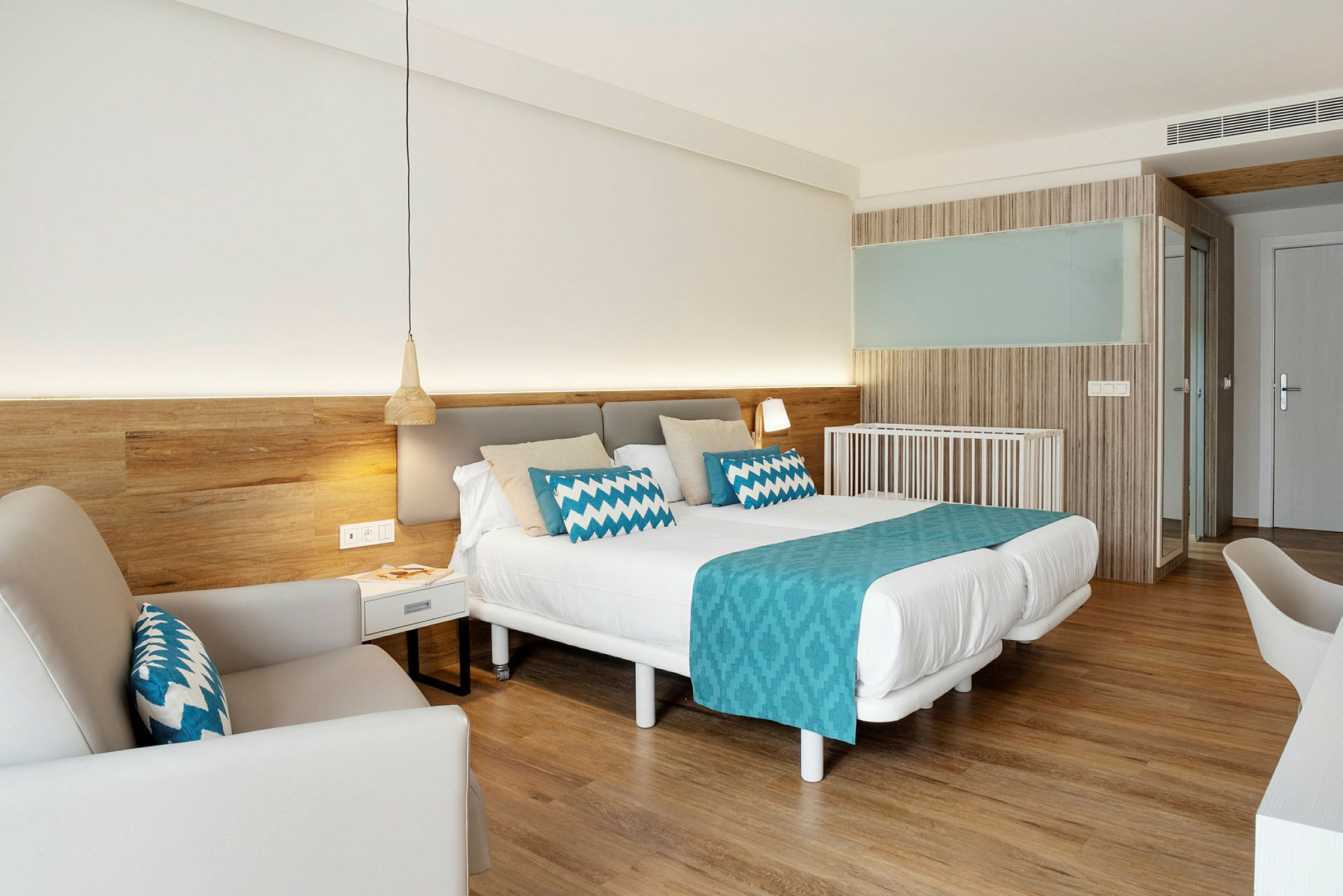 Ett väl belyst hotellrum med en dubbelsäng, blå dekorationer, och trädetaljer. (AI-genererad text)