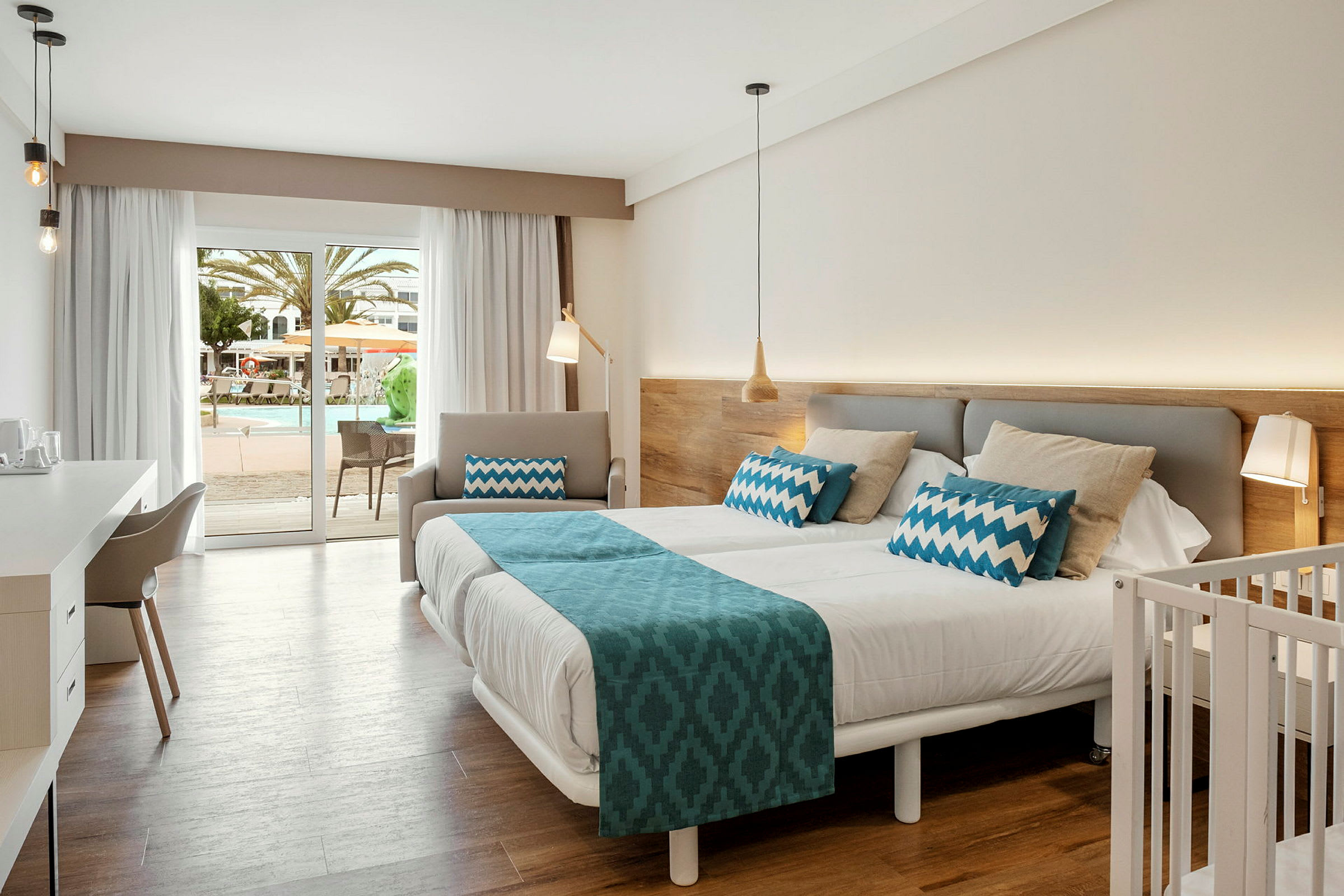 Hotellrum med dubbelsäng, barnmöbel, skrivbord och fönster mot poolområde. (AI-genererad text)