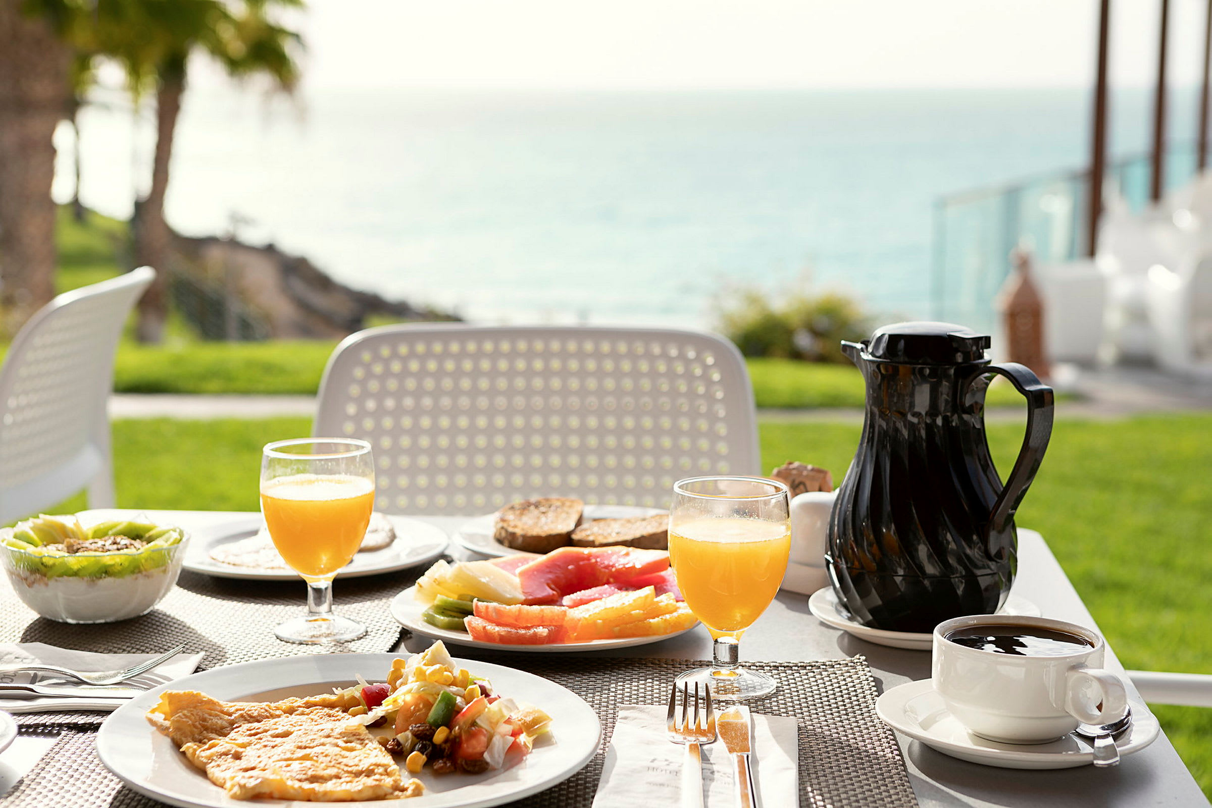 Ett bord med frukostmat utomhus, med utsikt mot havet. (AI-genererad text)