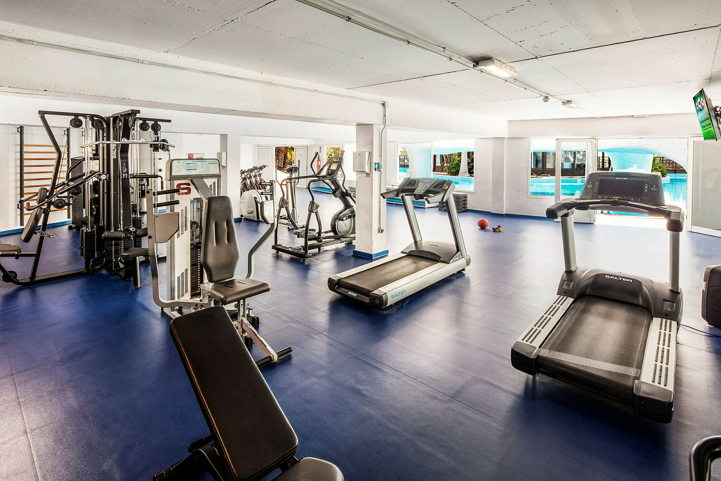 Gym med träningsmaskiner och löpband, blått golv. (AI-genererad text)