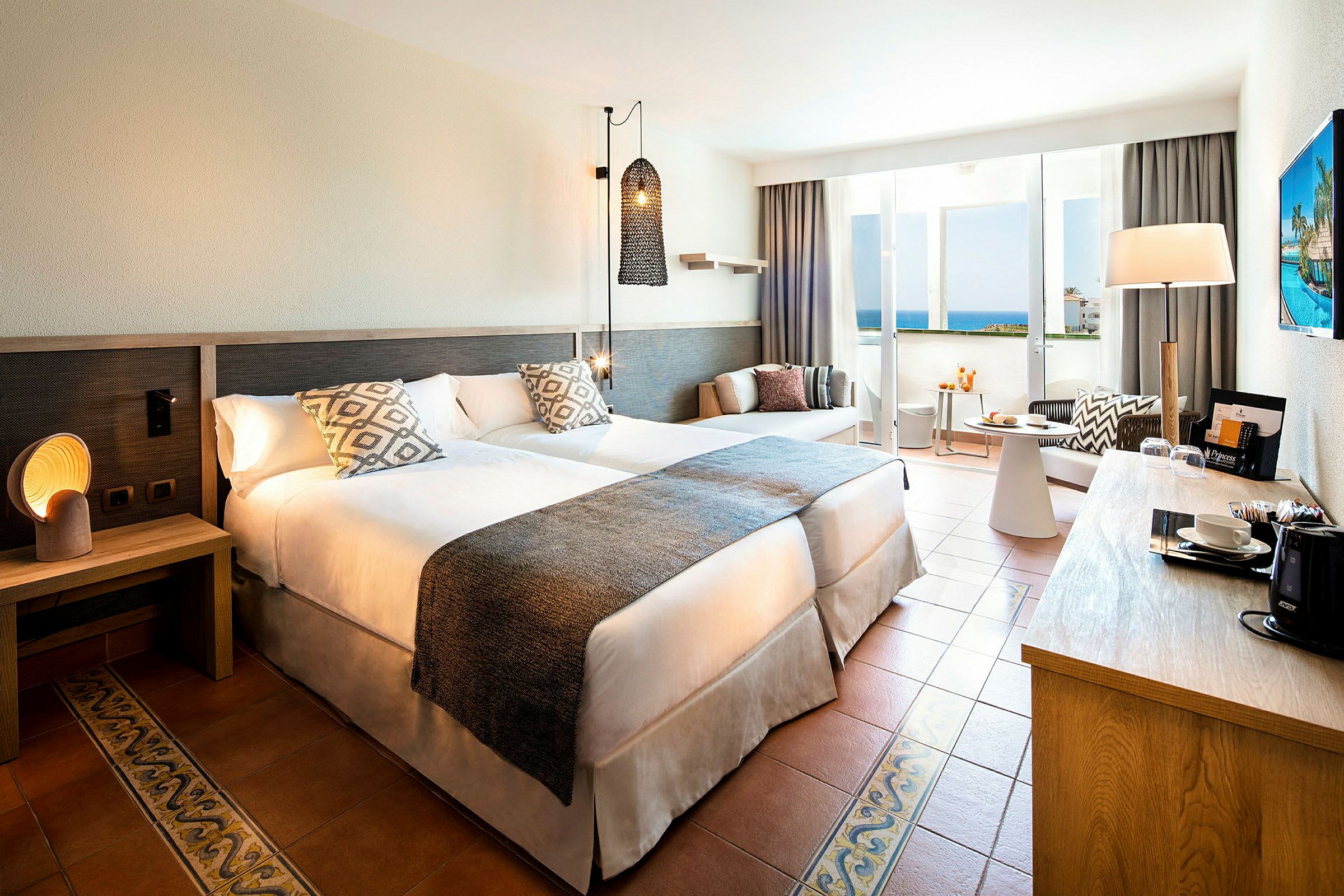 Hotellrum med två sängar, nattduksbord, sittgrupp och balkong med havsutsikt. (AI-genererad text)