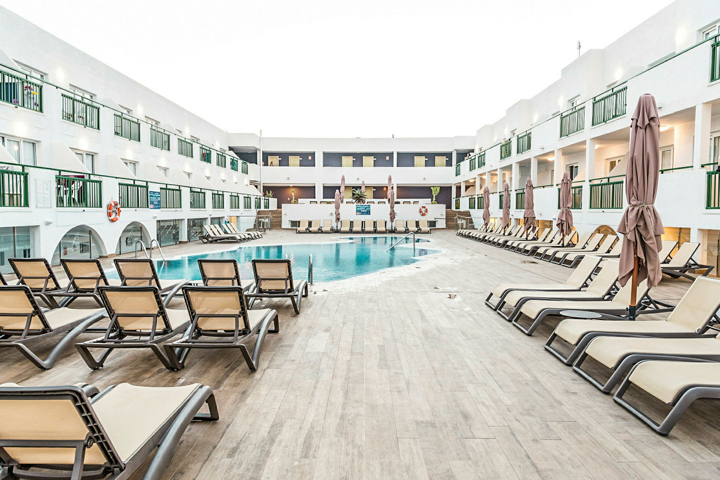 Bild som visar en pool omgiven av solstolar och ett hotellkomplex i bakgrunden. (AI-genererad text)
