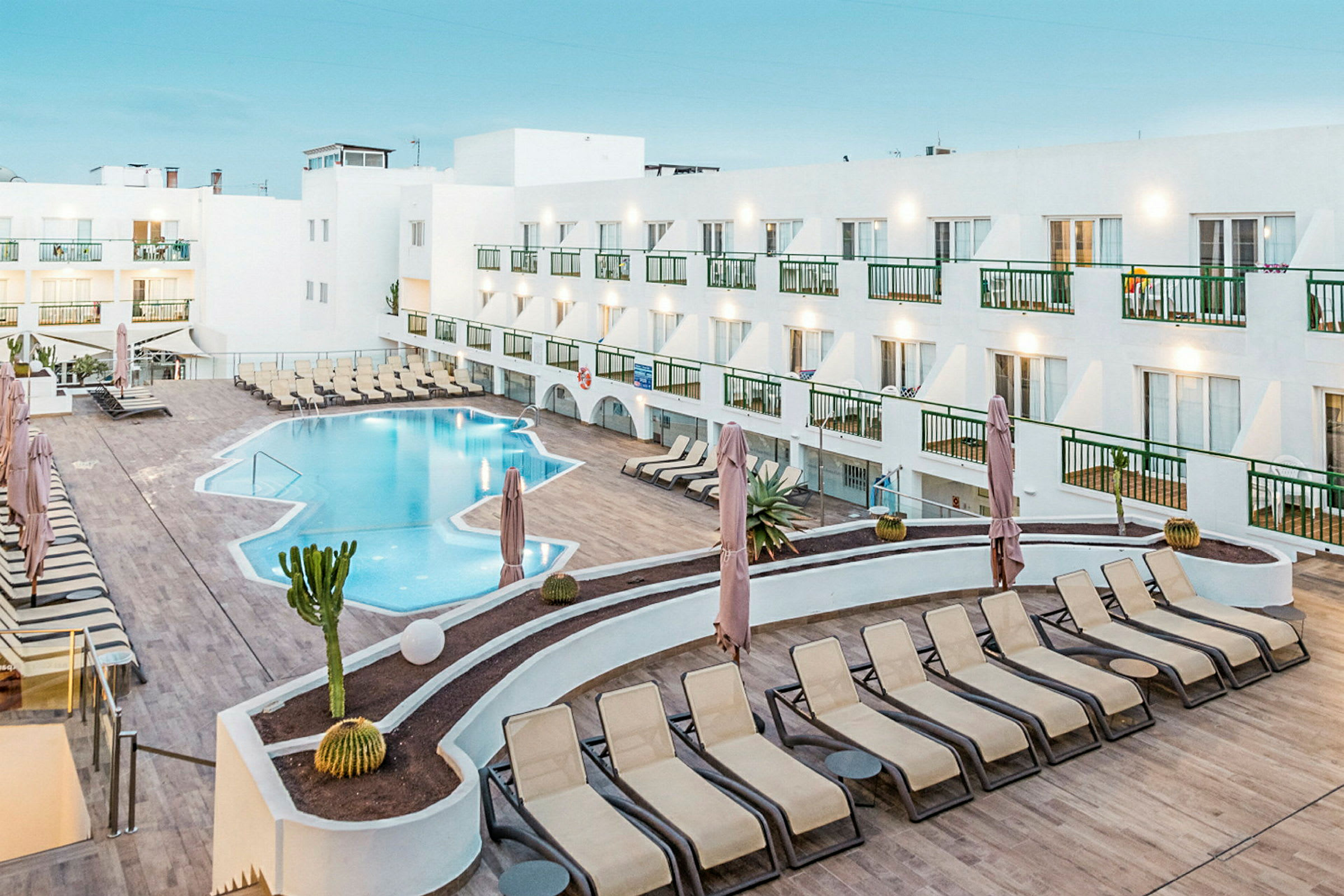 En hotellpool med solsängar och vit byggnad runtom. (AI-genererad text)