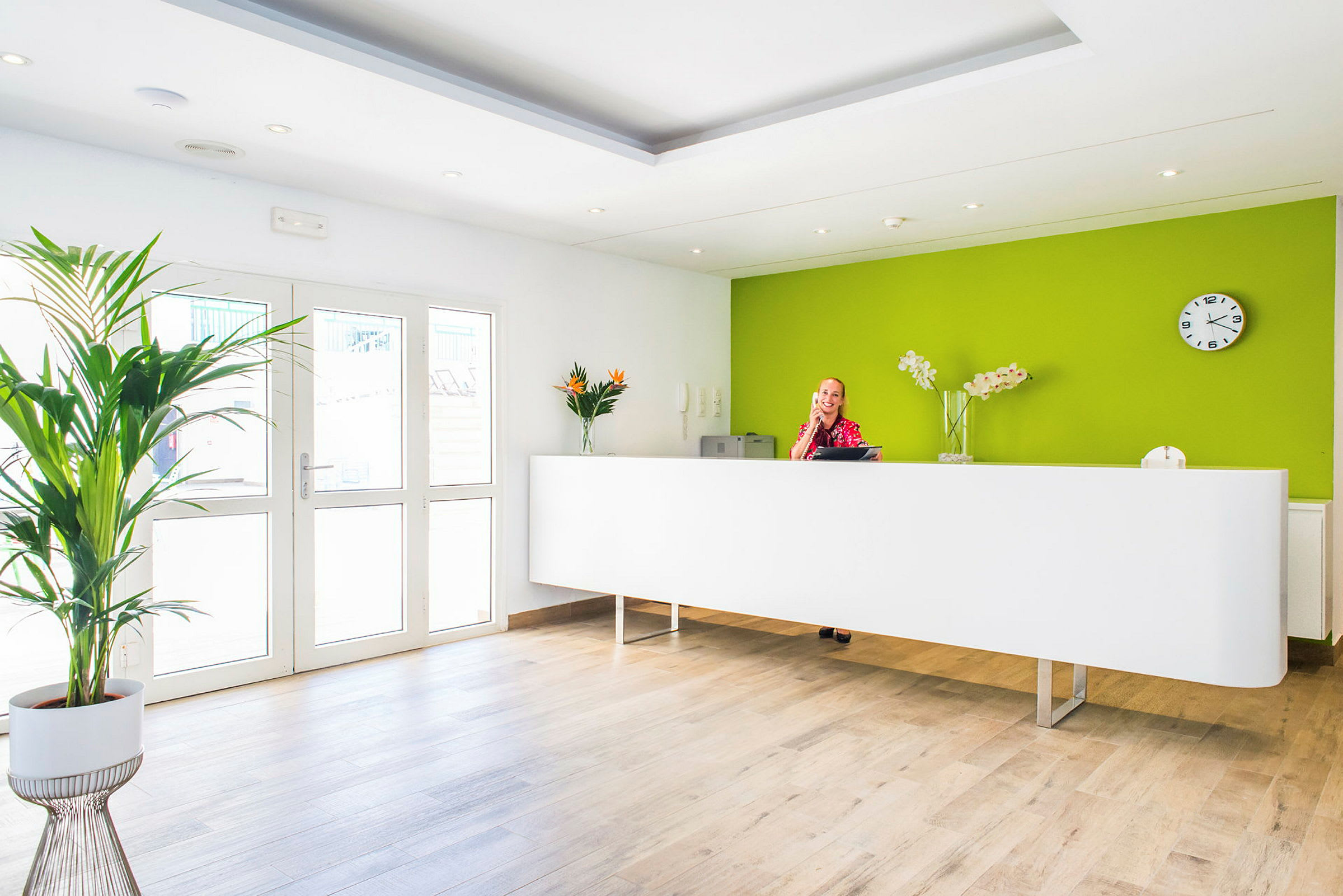 Reception med vit disk, grön vägg och dekorationer som blommor och en klocka. (AI-genererad text)