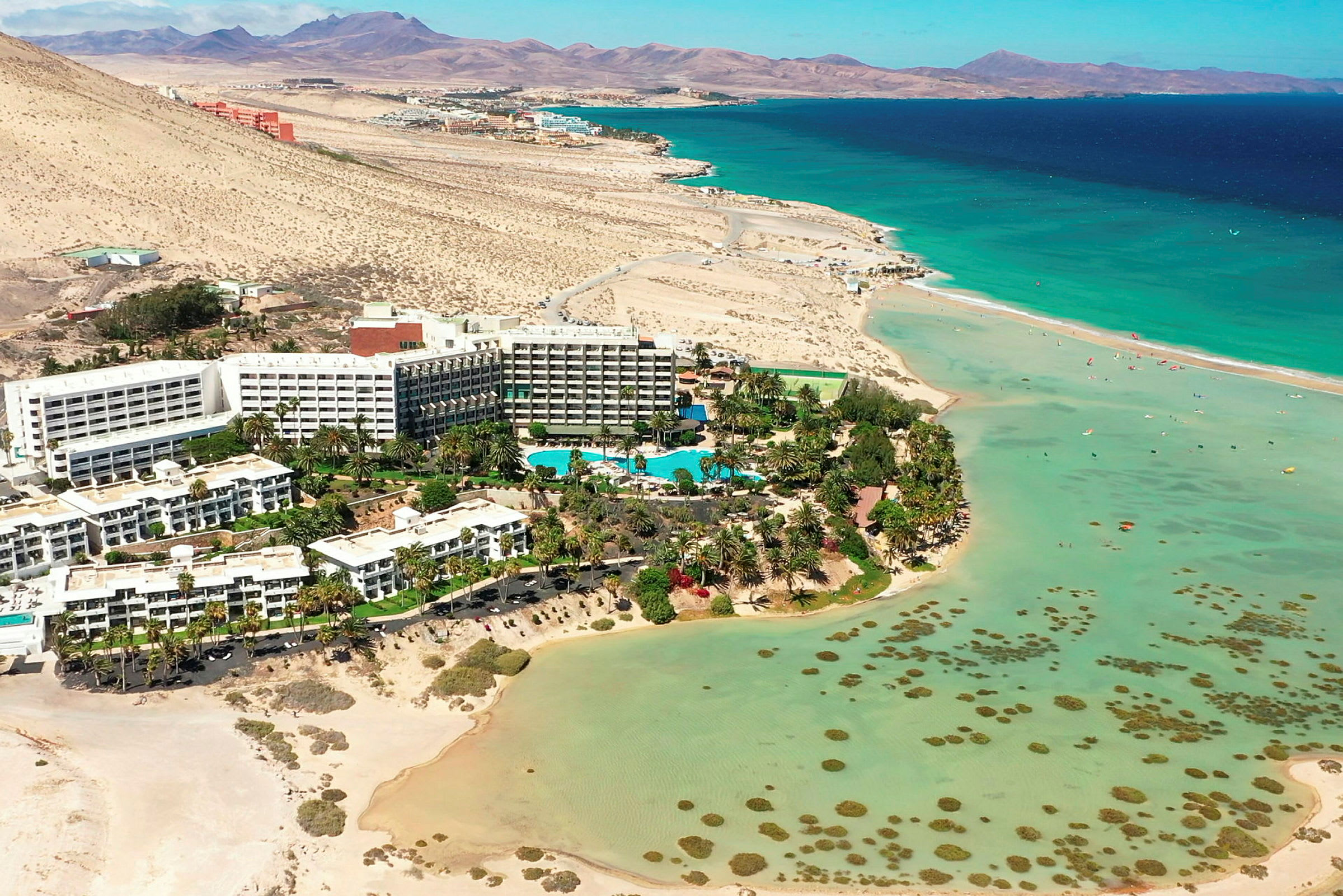 Hotellkomplex vid en strand med turkost vatten och omgivande ökenlandskap. (AI-genererad text)