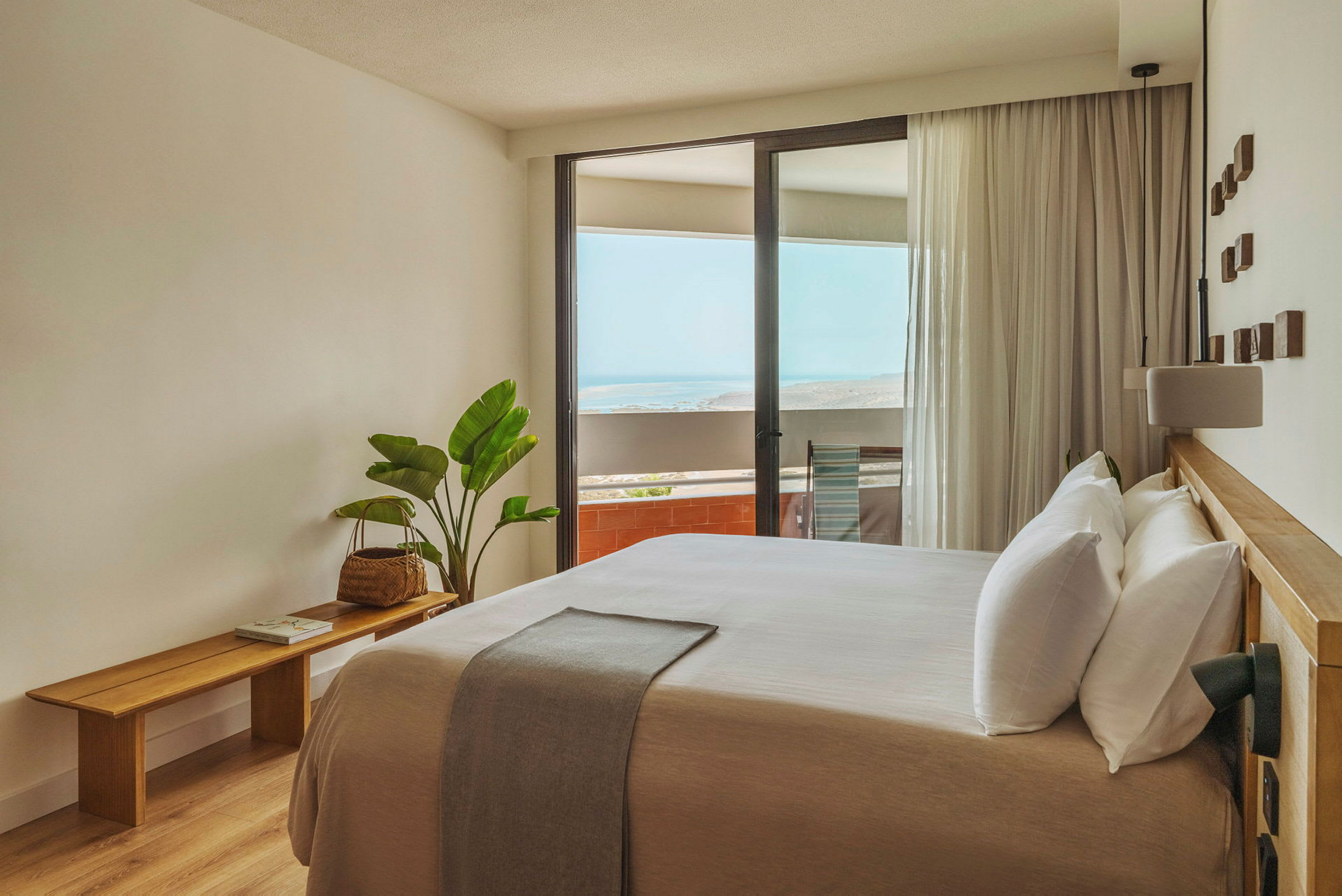 Ett ljust och modernt inrett hotellrum med en stor säng och en balkong som har utsikt över havet. (AI-genererad text)