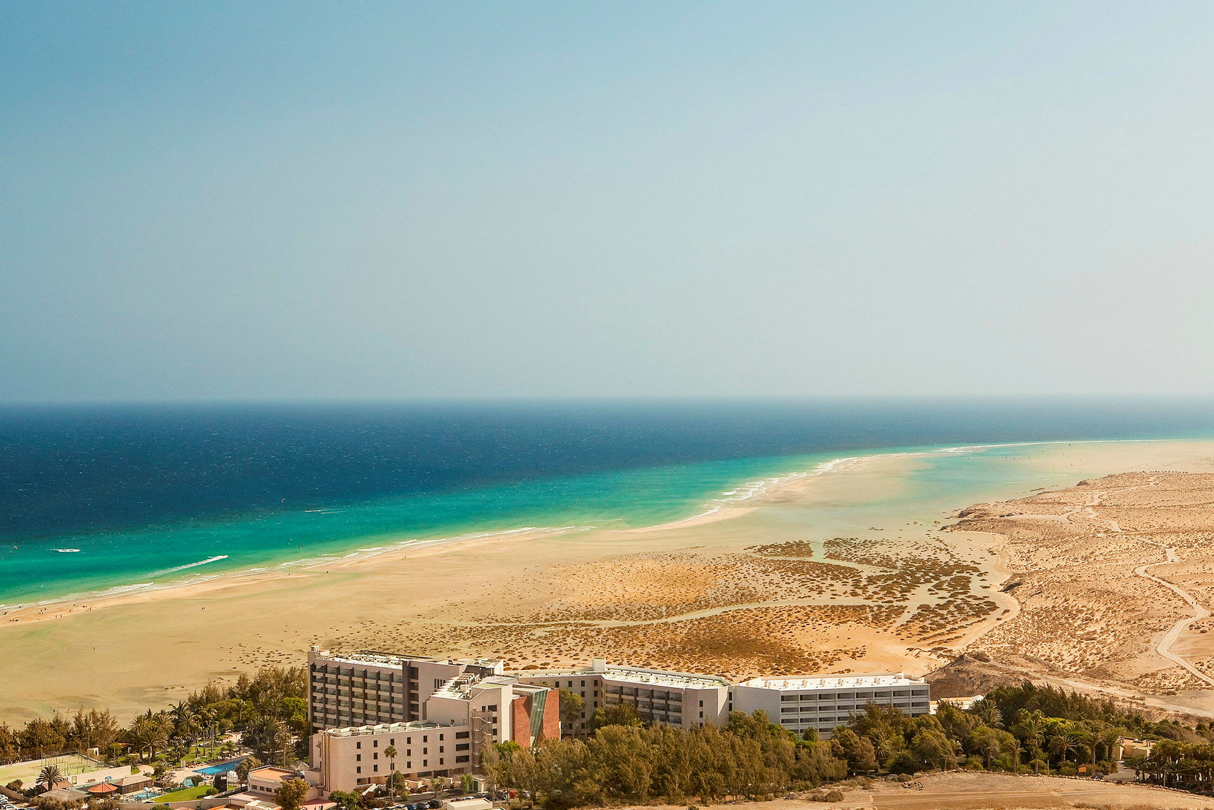 Hotell framför en vidsträckt sandstrand och turkost hav. (AI-genererad text)