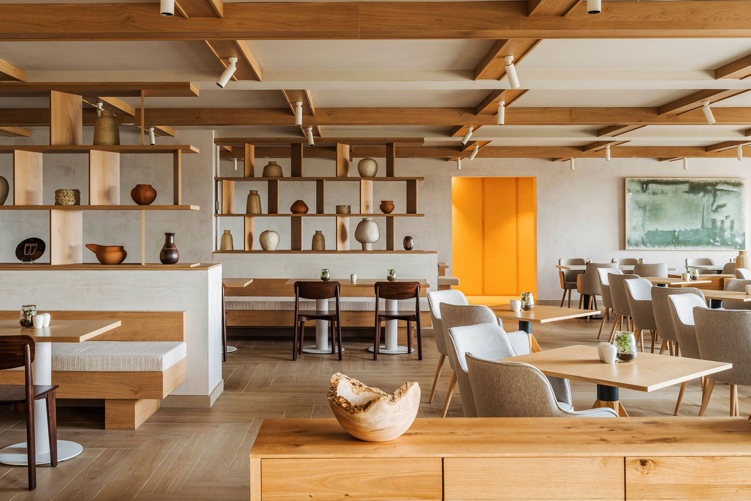 Ett modernt café eller restaurang med träinredning, hyllor med keramiska föremål och flera bord och sittplatser. (AI-genererad text)