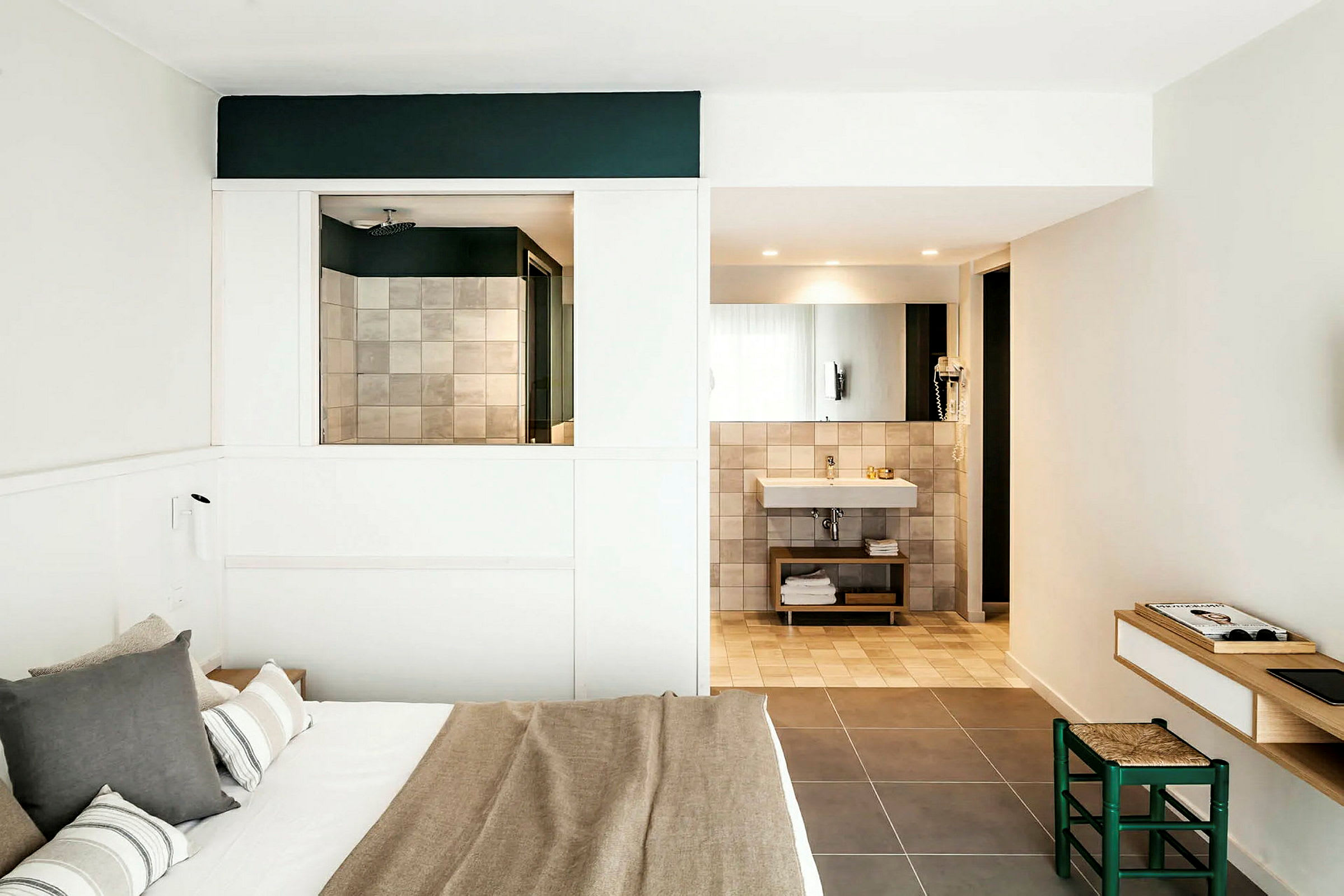 Ett modernt hotellrum med en dubbelsäng, badrum med spegel och handfat samt en liten arbetsyta med stol. (AI-genererad text)