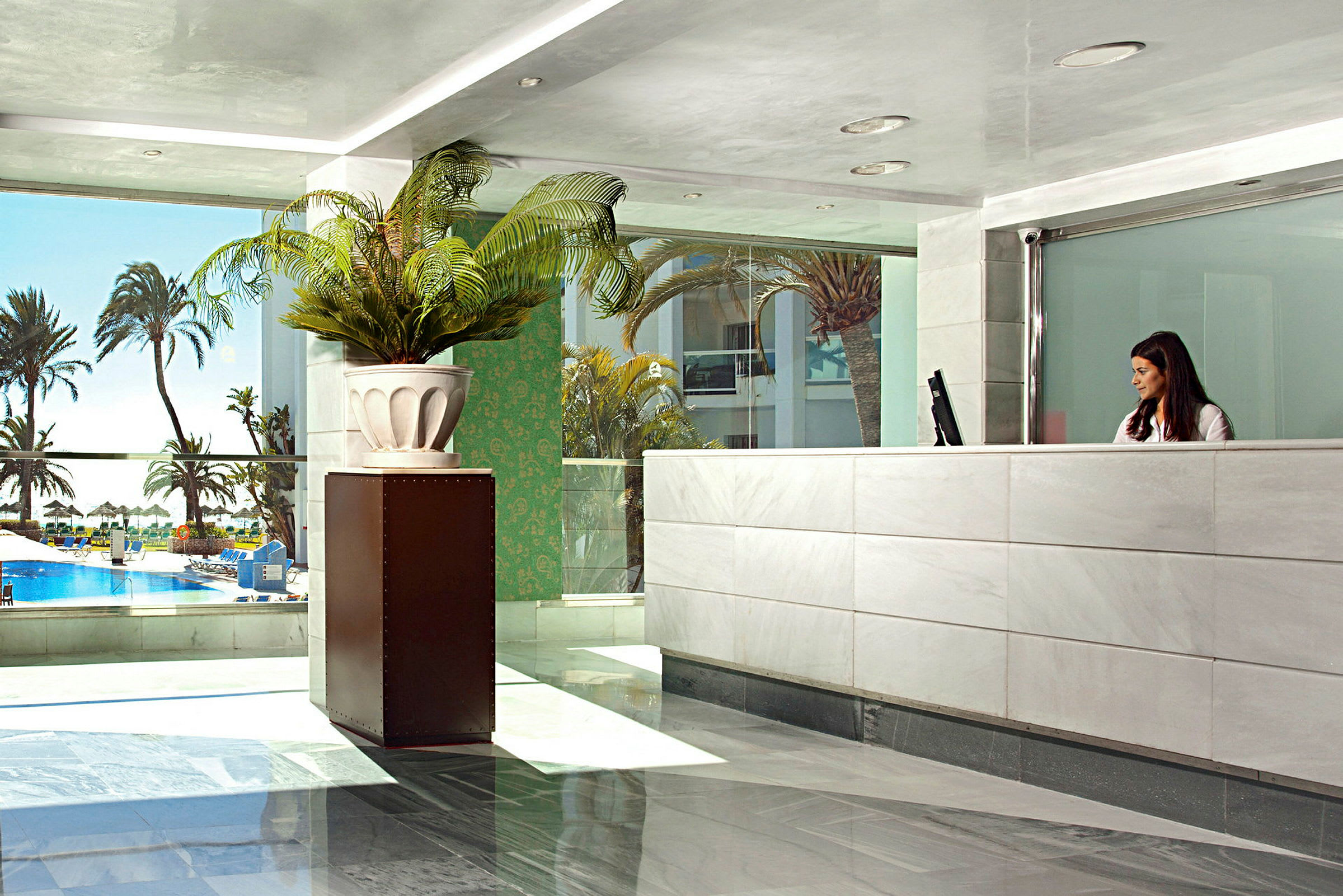 Reception med modern inredning och utsikt över ett poolområde och palmer utanför. (AI-genererad text)