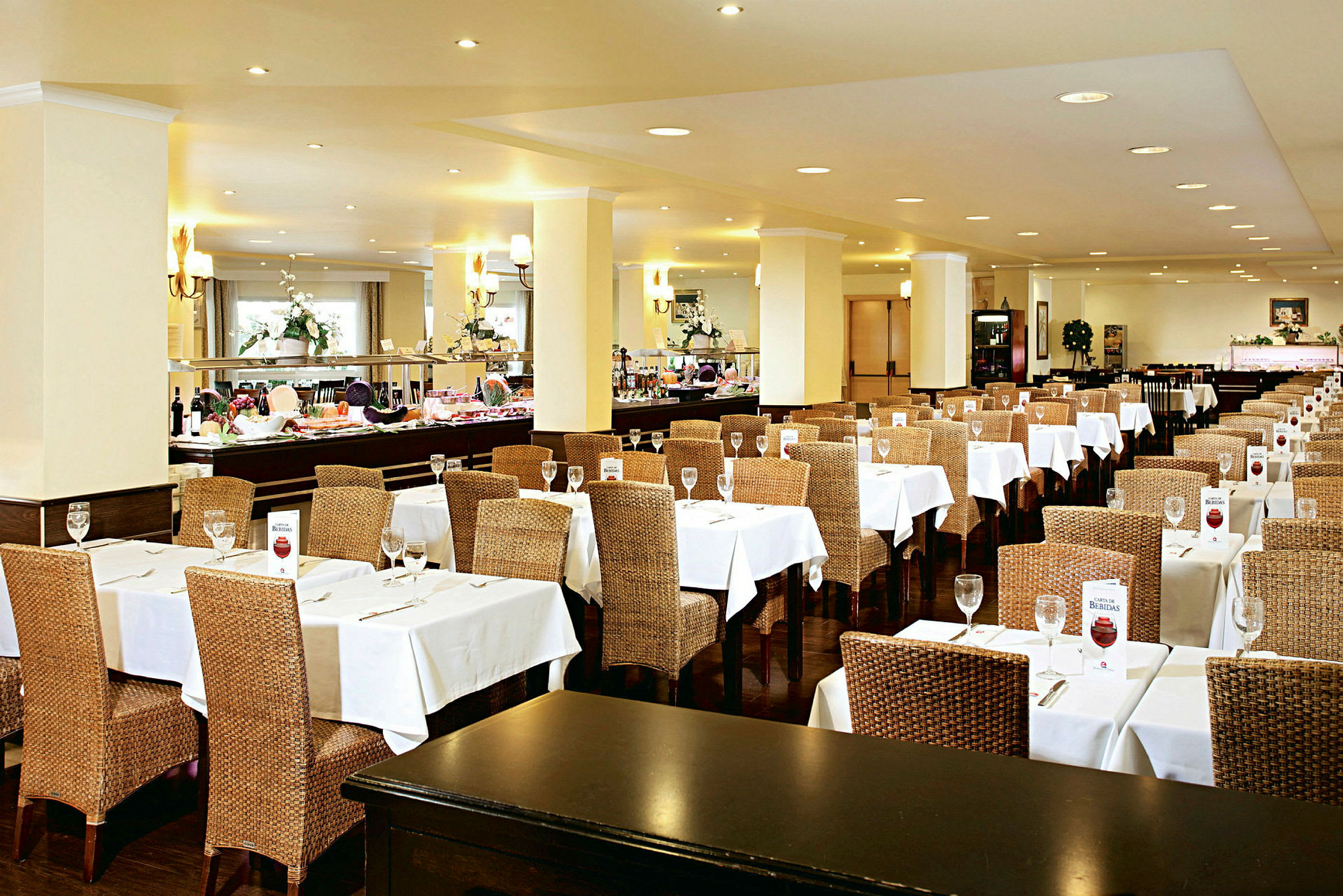 En restaurang med dukade bord och stolar med flätad design. Buffébord syns i bakgrunden. (AI-genererad text)