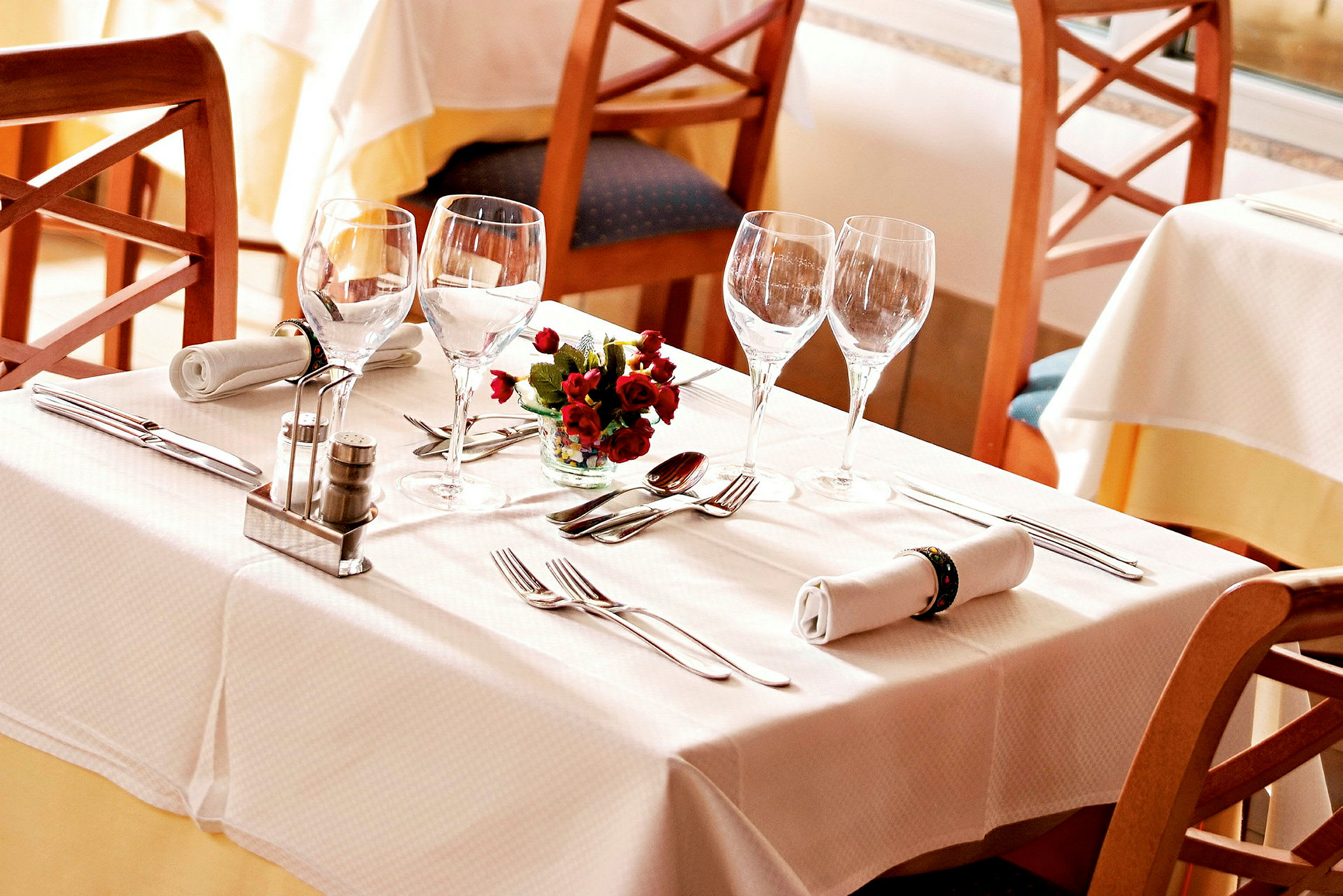 Ett dukat bord med vita dukar, glas, bestick, servetter och en liten blomdekoration. (AI-genererad text)