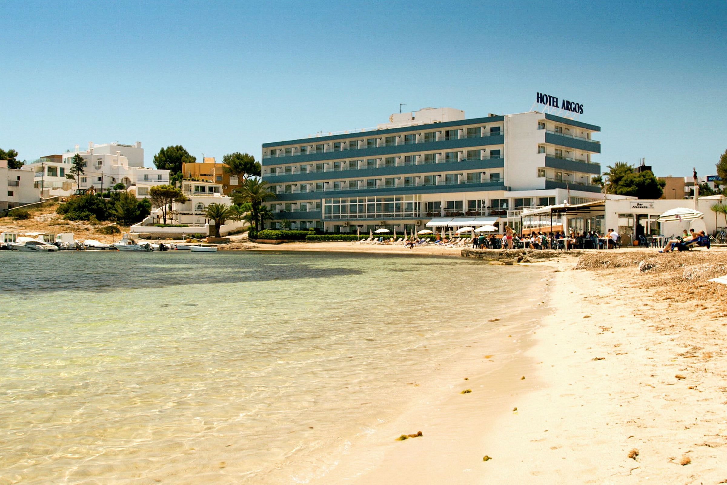 Strand med klart vatten framför ett hotell och byggnader. (AI-genererad text)