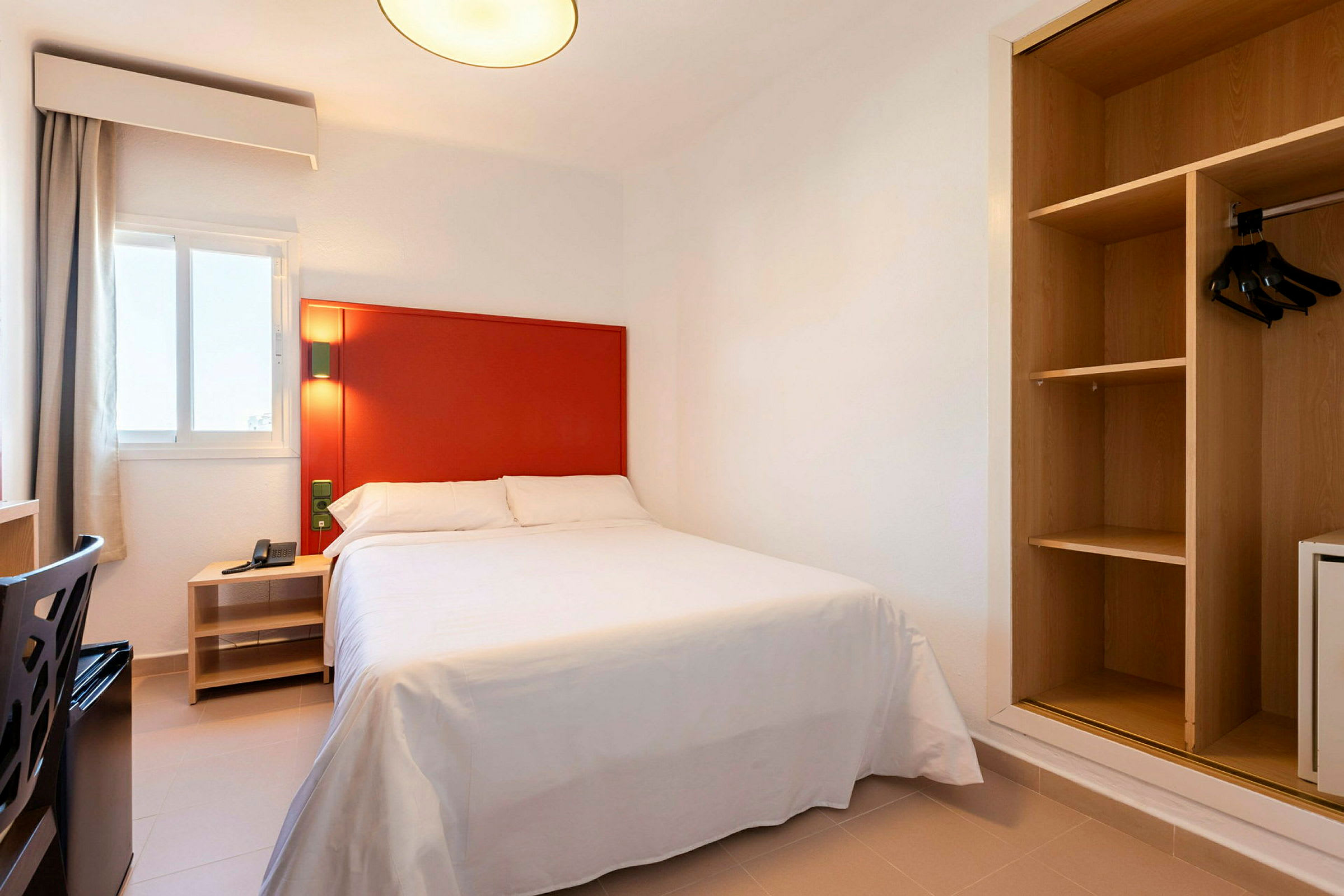 Bild av ett hotellrum med en säng, röd sänggavel och öppen garderob. (AI-genererad text)