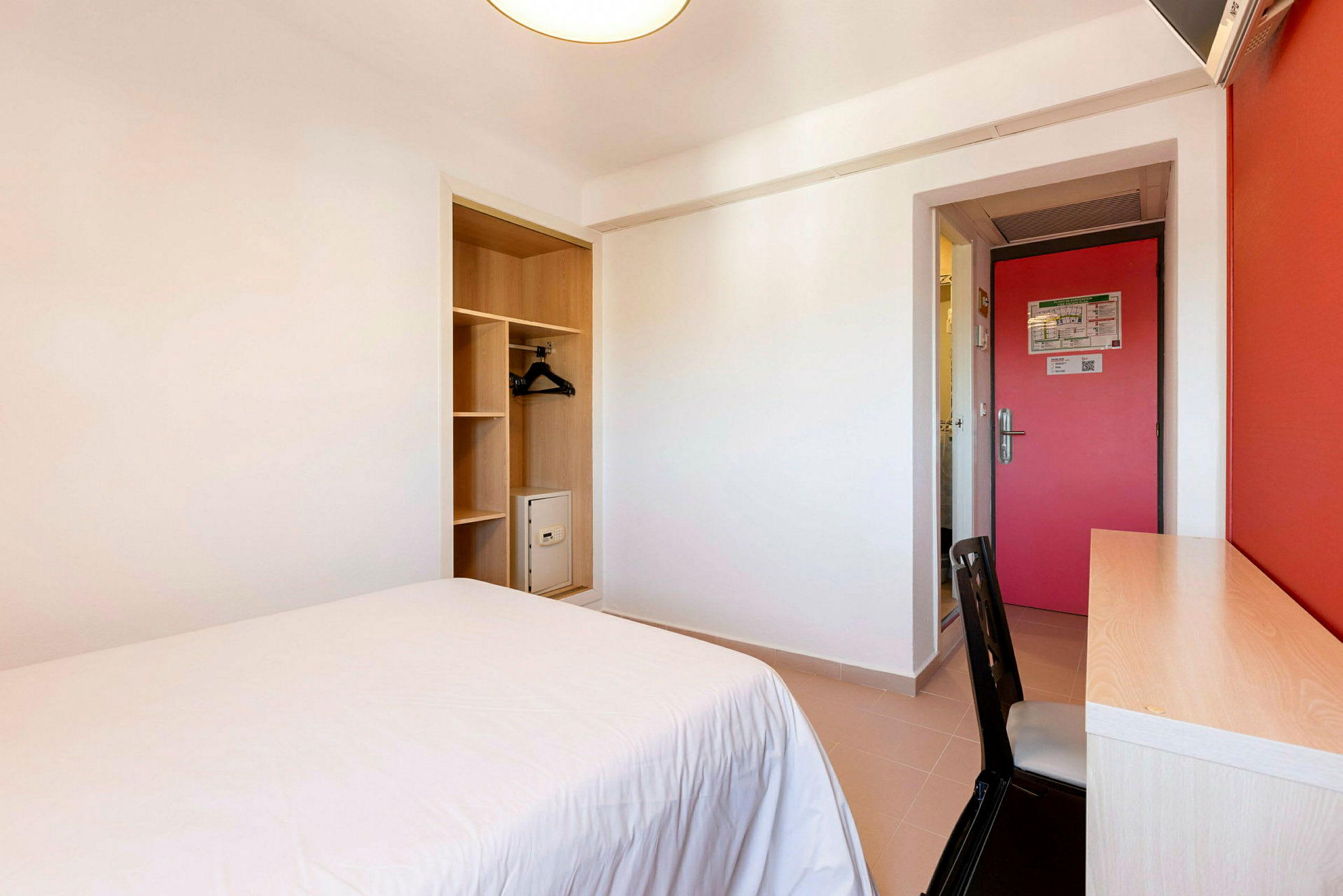 Ett hotellrum med en säng, skrivbord och garderob. (AI-genererad text)
