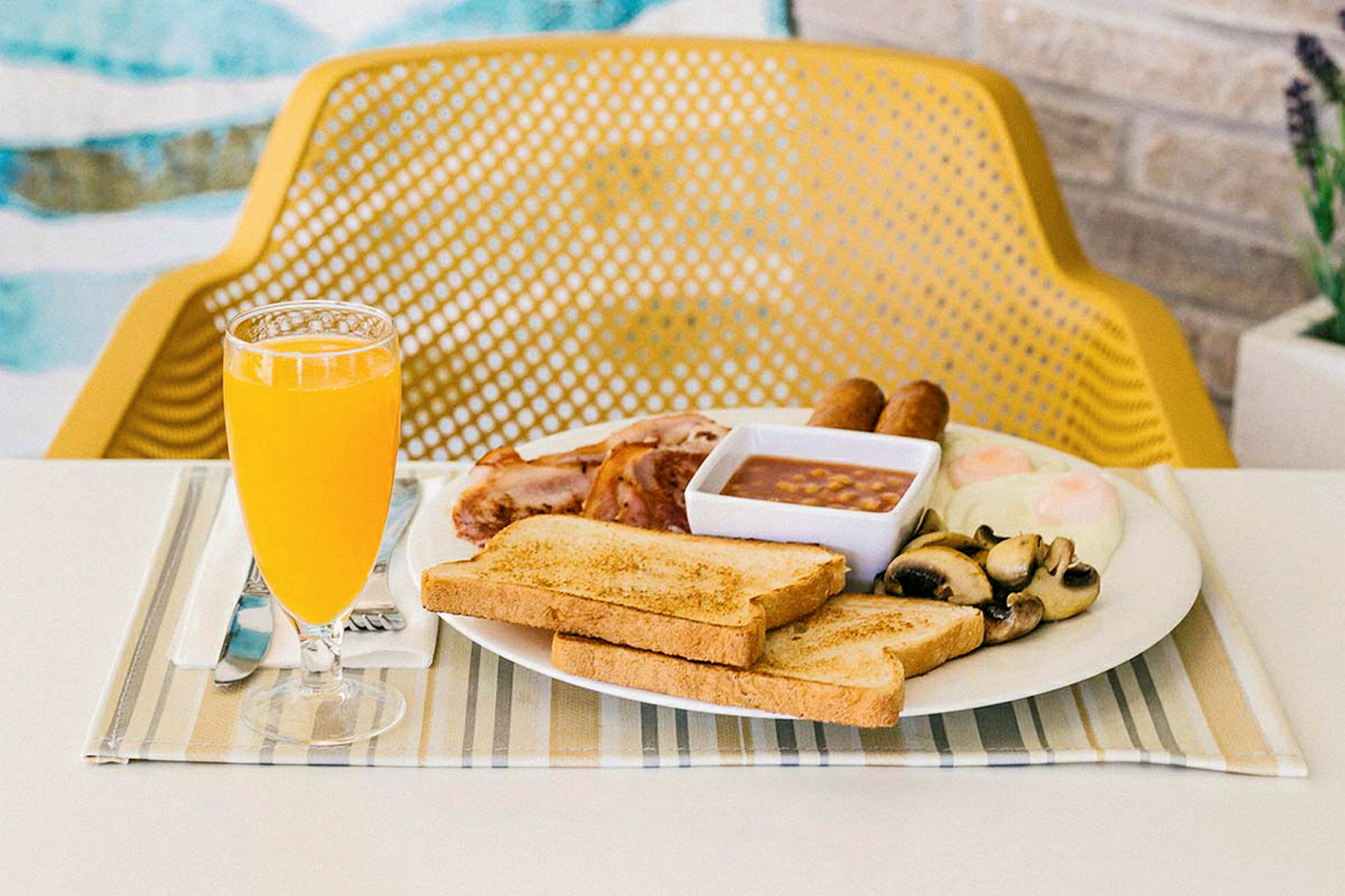 Frukost med rostat bröd, stekta ägg, korv, bönor, svamp och apelsinjuice serverad vid ett bord. (AI-genererad text)