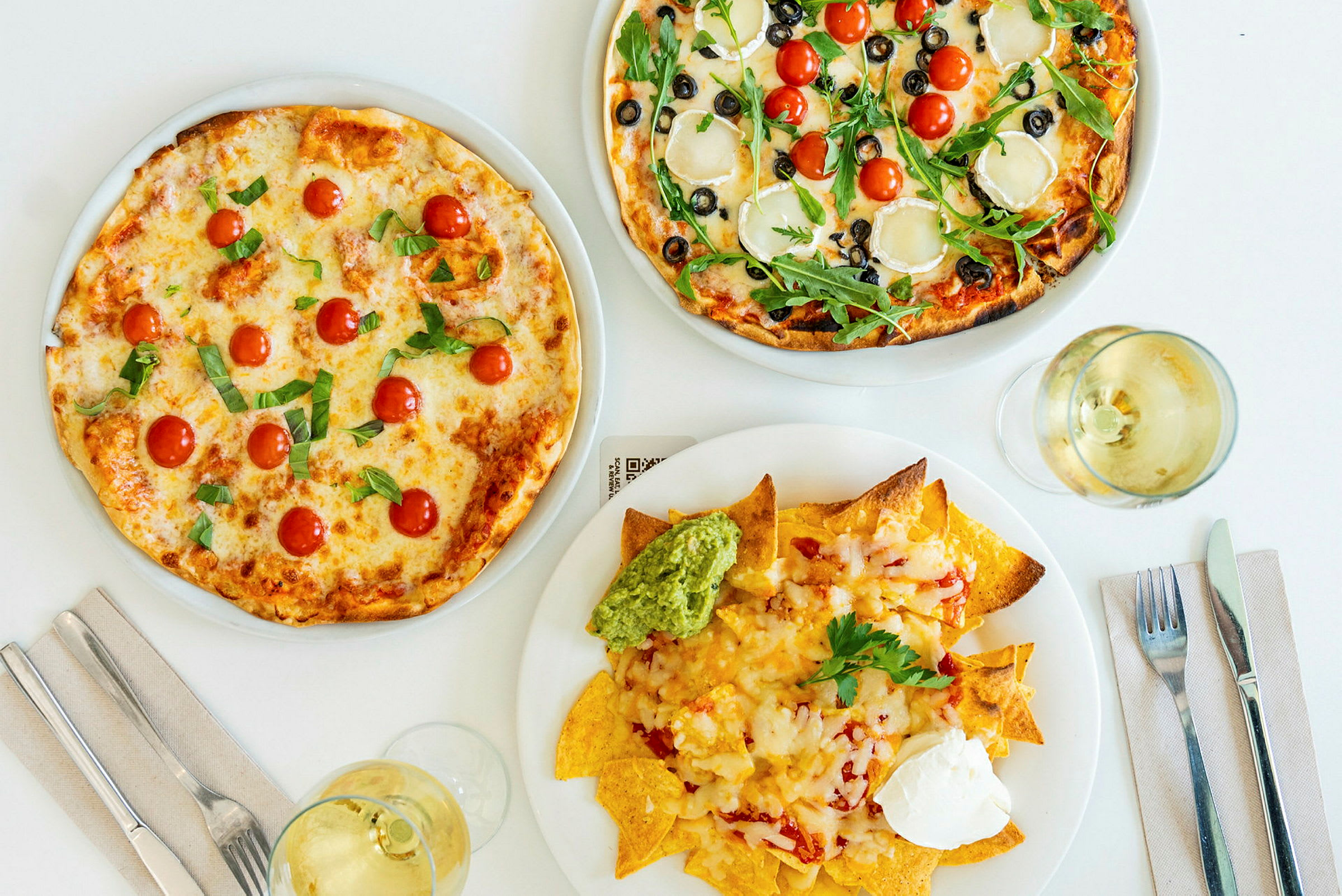 Två pizzor med olika toppings och en tallrik nachos med guacamole och gräddfil. (AI-genererad text)