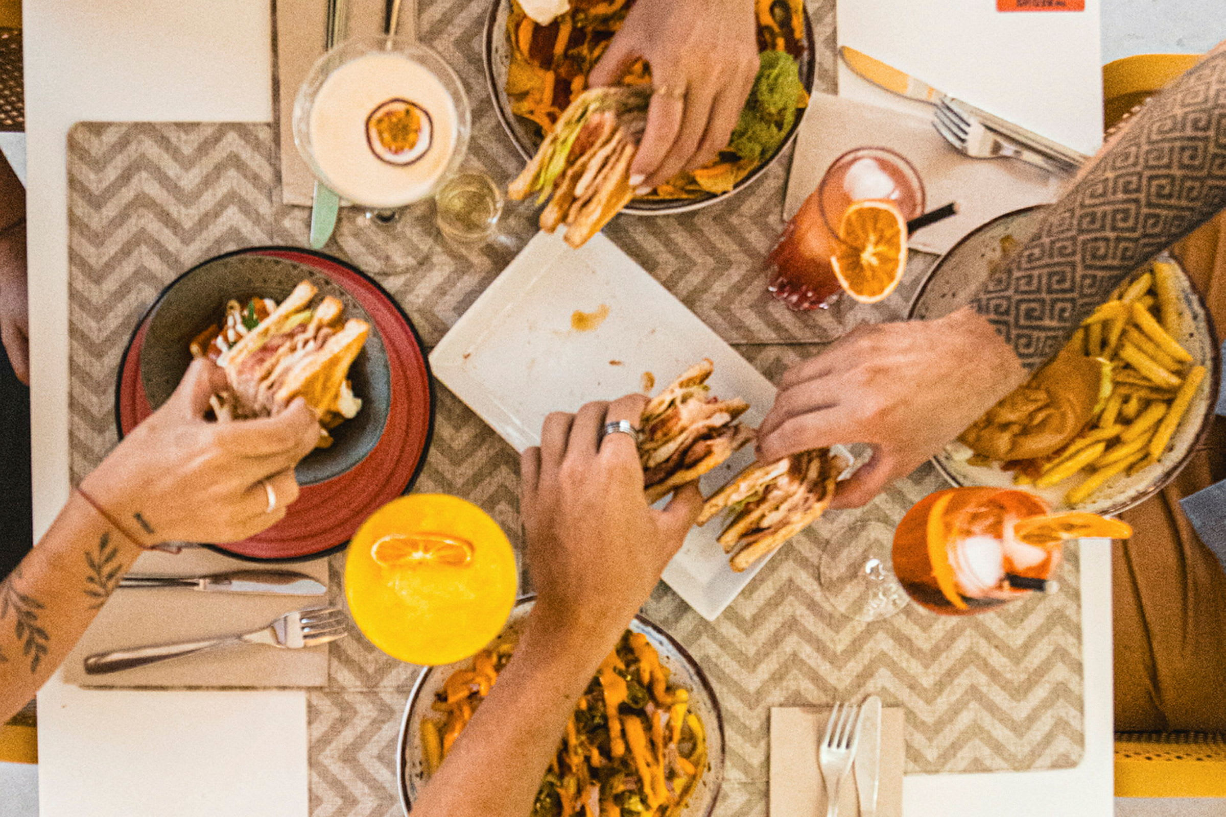 Fyra personer äter hamburgare, pommes frites och dricker färgglada drycker vid ett bord. (AI-genererad text)