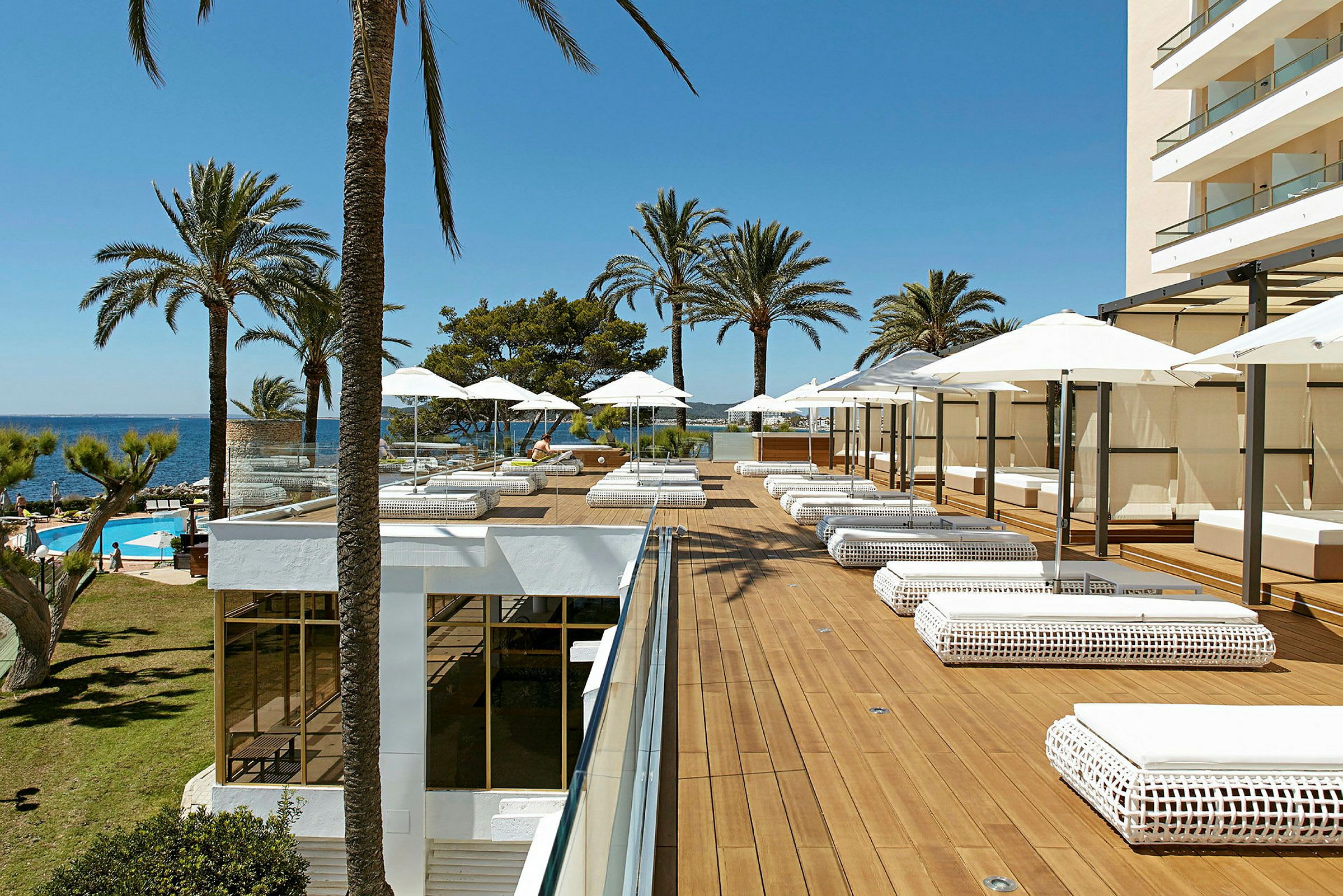 En hotellterrass med solbäddar och parasoller, omgiven av palmer och utsikt mot havet. (AI-genererad text)