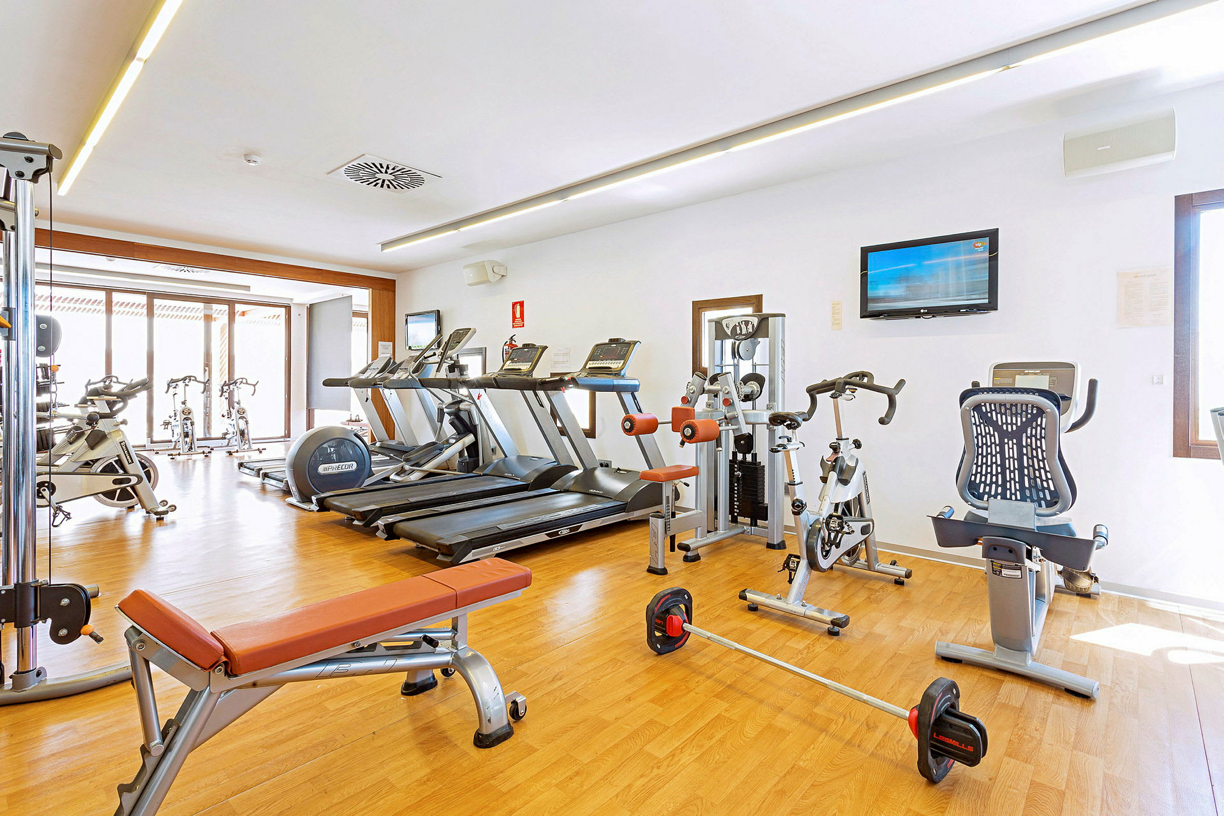 Ett gym med löpband, träningscyklar och träningsmaskiner på ett ljust trägolv. (AI-genererad text)