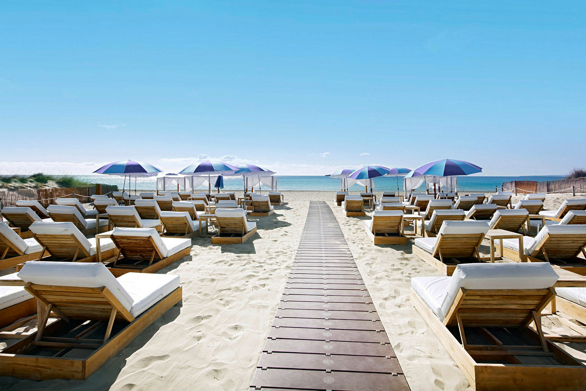 Solstolar och strandparaplyer på en sandstrand med havsutsikt. (AI-genererad text)