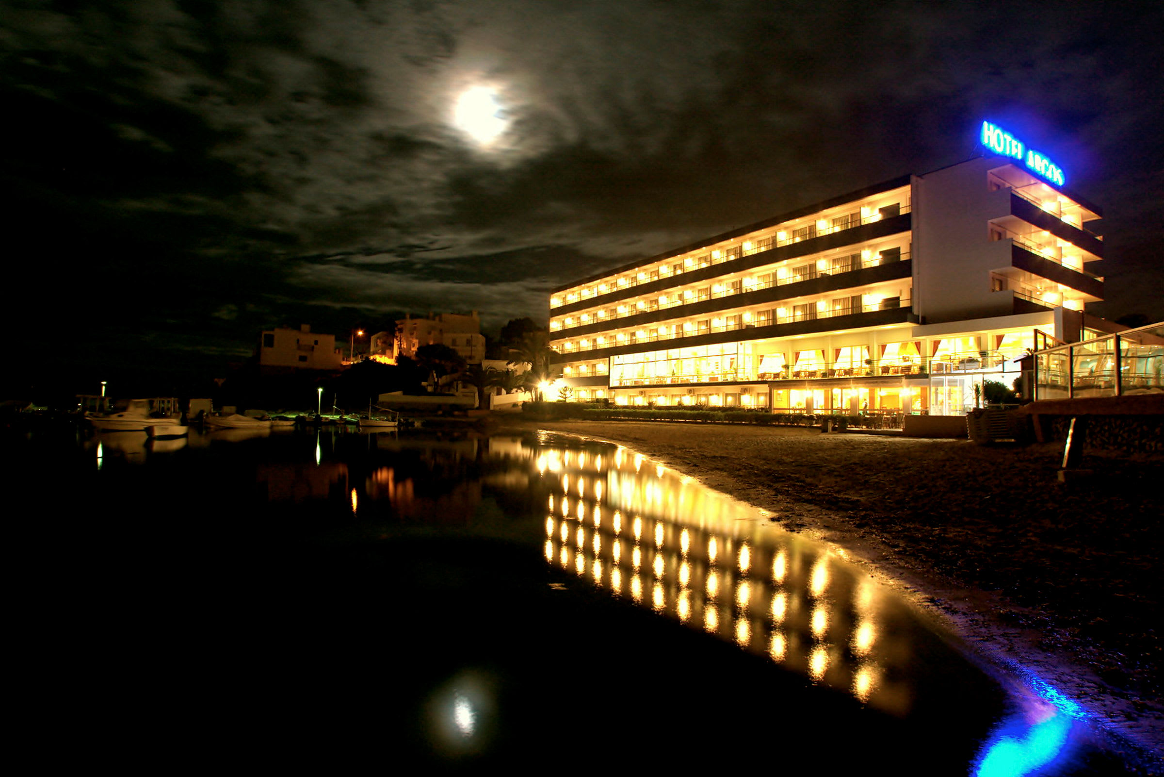 Ett hotell upplyst på natten med en spegelbild i vattnet framför. (AI-genererad text)