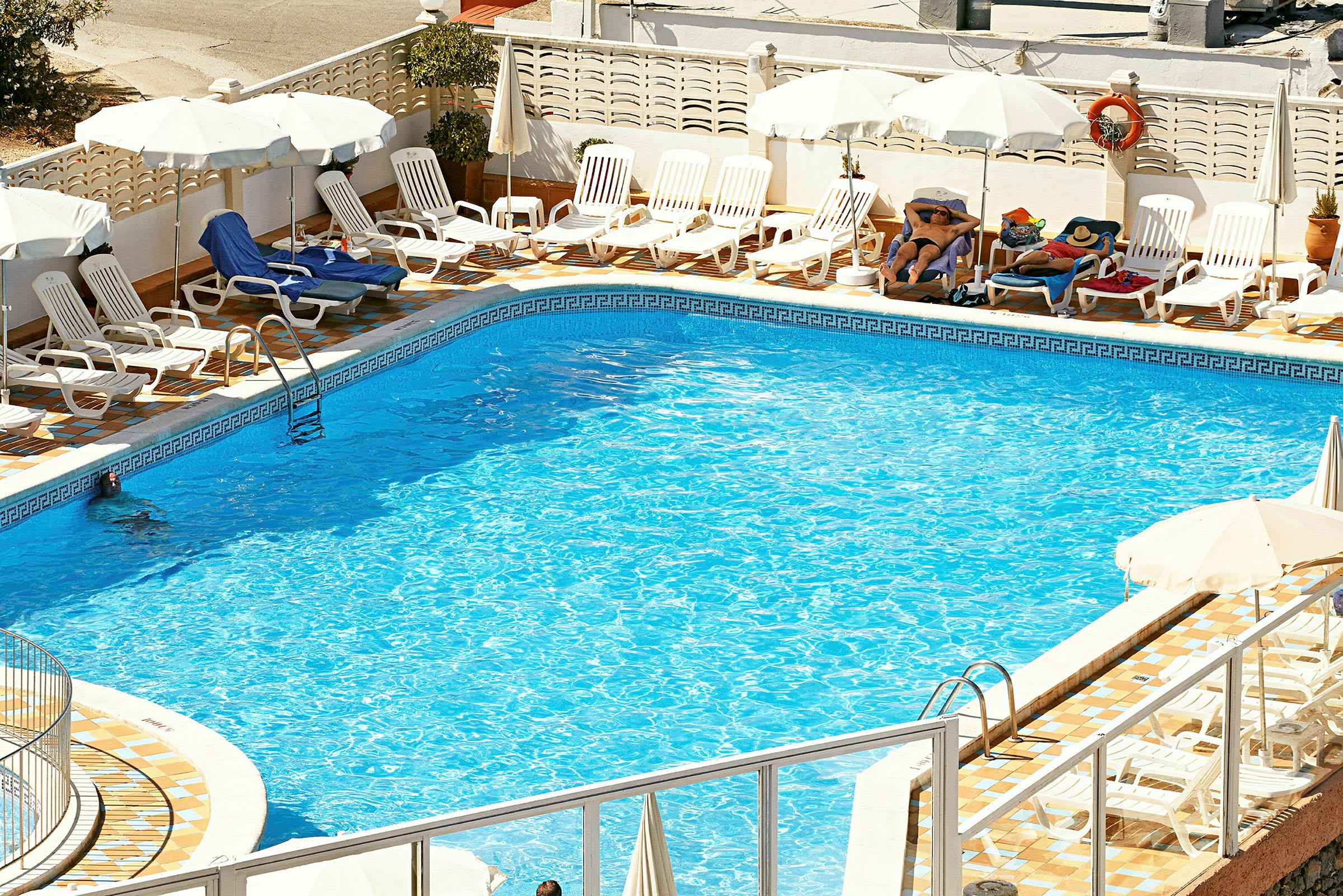 En swimmingpool utomhus med solsängar och parasoller runtom. (AI-genererad text)