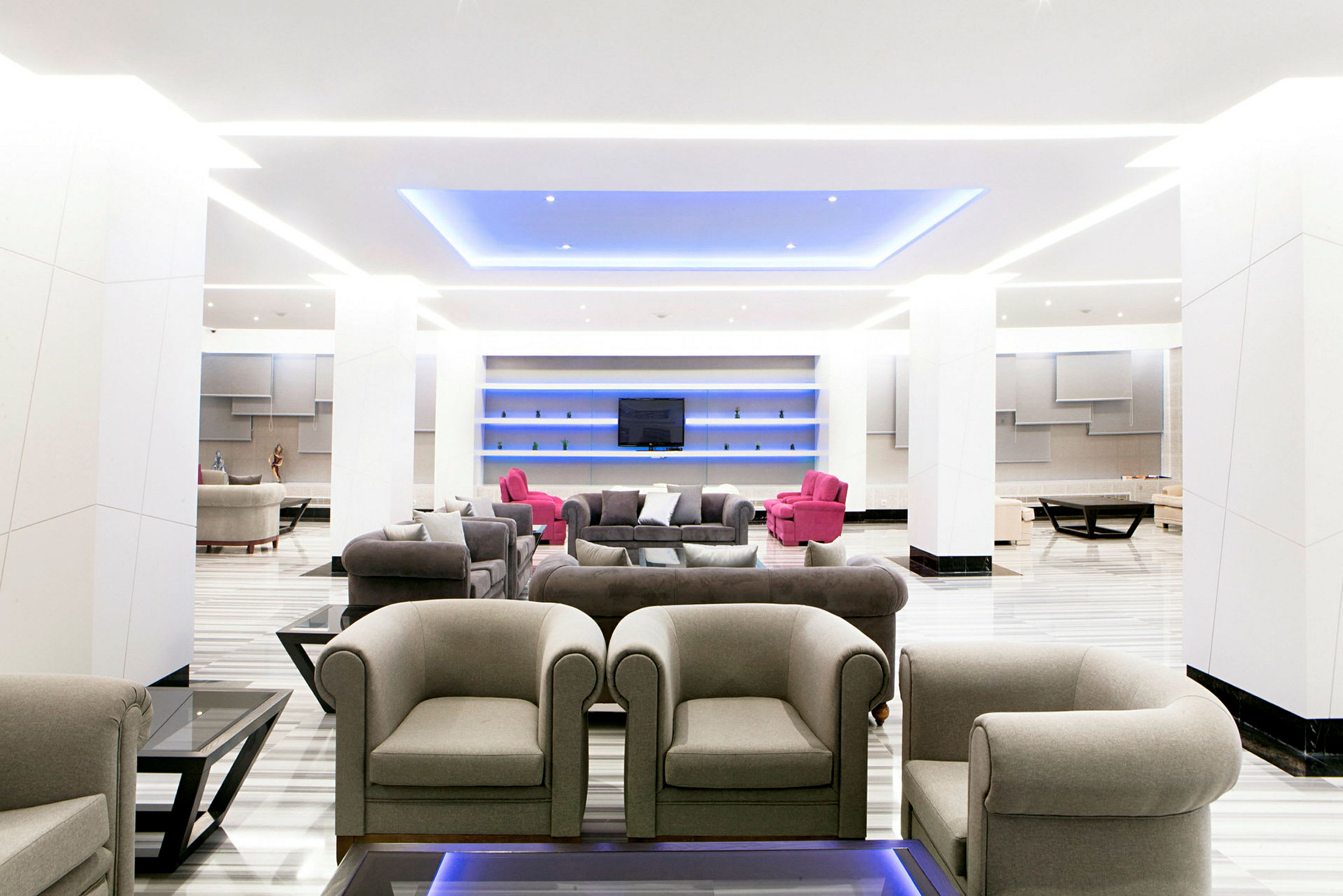 En modern lounge med grå och rosa sittmöbler samt ett blått takljus. (AI-genererad text)