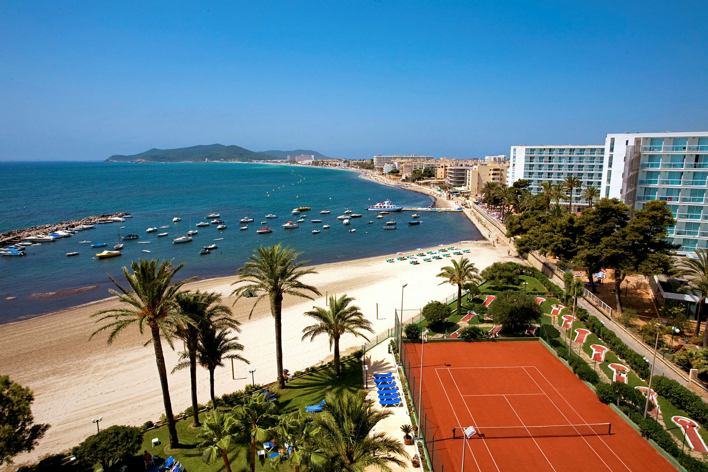 Flygfoto av en strand med palmer, en pool och en plats för tennis. (AI-genererad text)