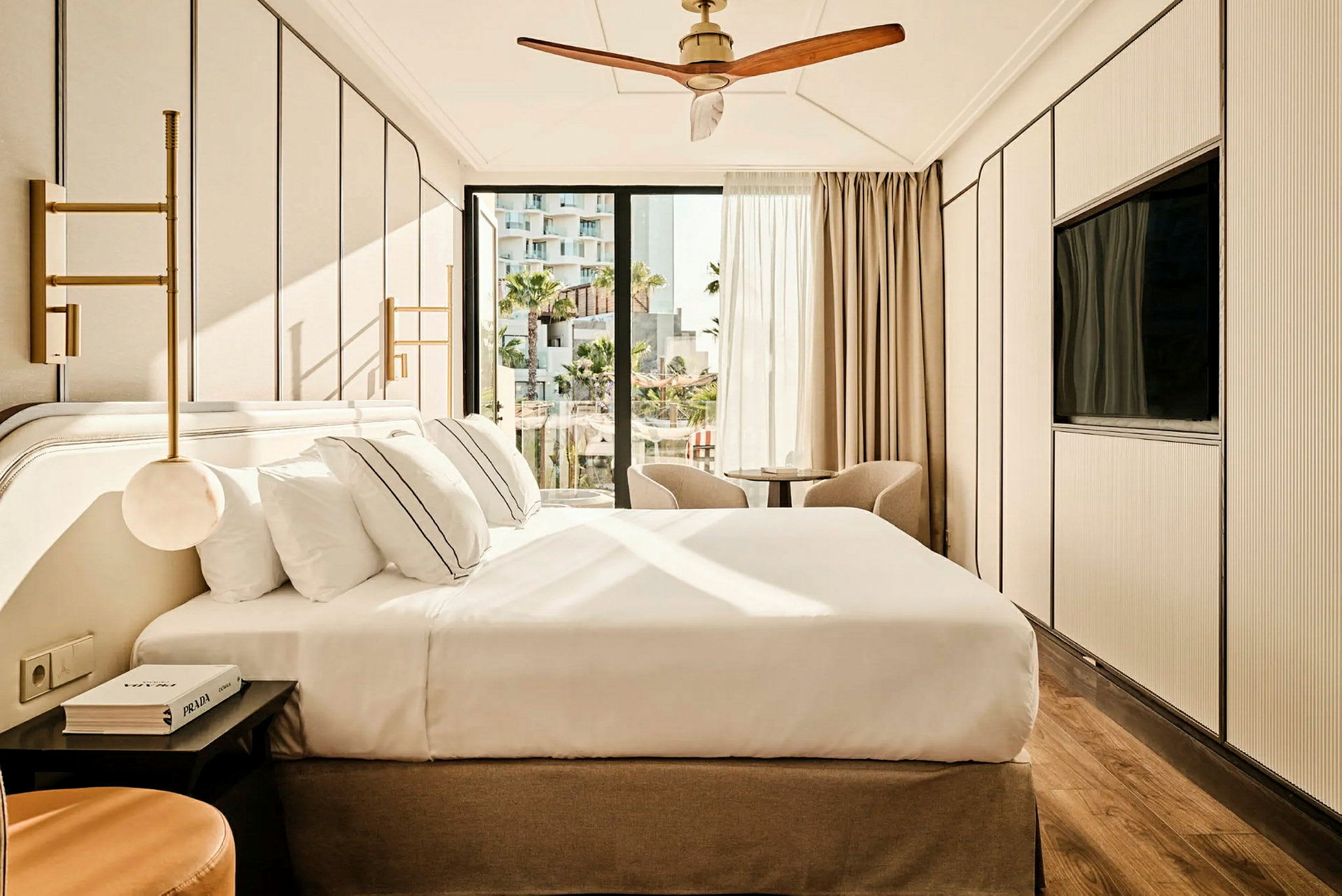 Ett modernt hotellrum med en stor säng, två fåtöljer framför fönstret och en takfläkt. (AI-genererad text)
