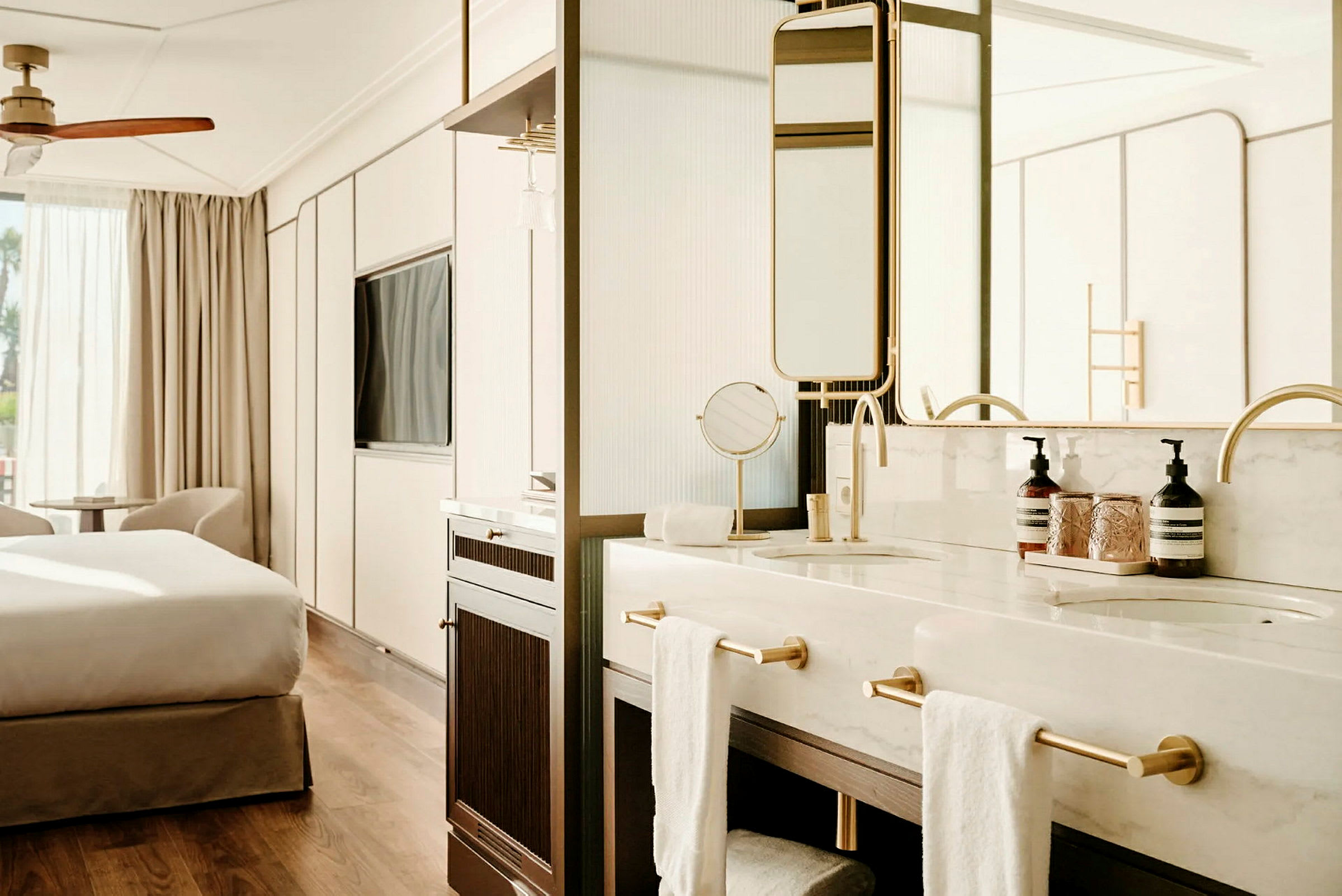 Ett elegant hotellrum med ett sovutrymme och ett öppet badrum med två handfat och guldfärgade armaturer. (AI-genererad text)
