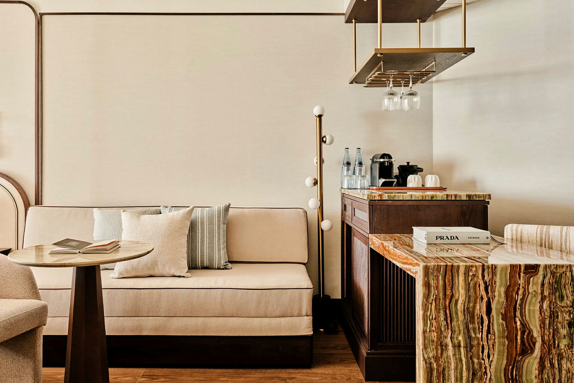En elegant inredd sittgrupp med en soffa, ett litet bord och en bänk med ett marmorerat skiva samt en kaffebryggare och glas. (AI-genererad text)