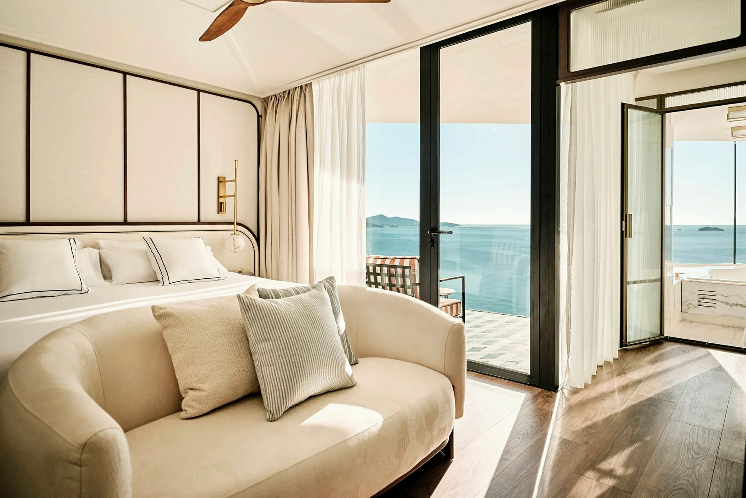 Modernt inrett hotellrum med stor säng, soffa och utsikt över havet från en balkong. (AI-genererad text)
