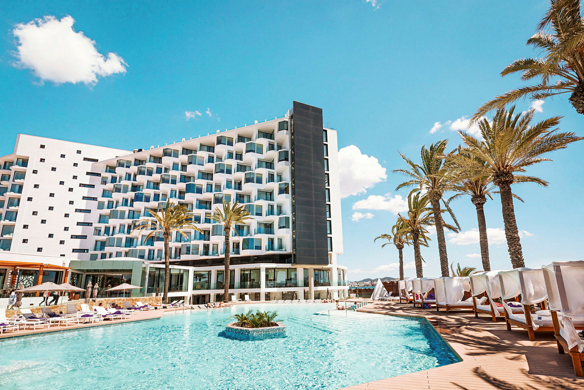 Hotell med pool och solsängar, omgivna av palmer under en blå himmel. (AI-genererad text)