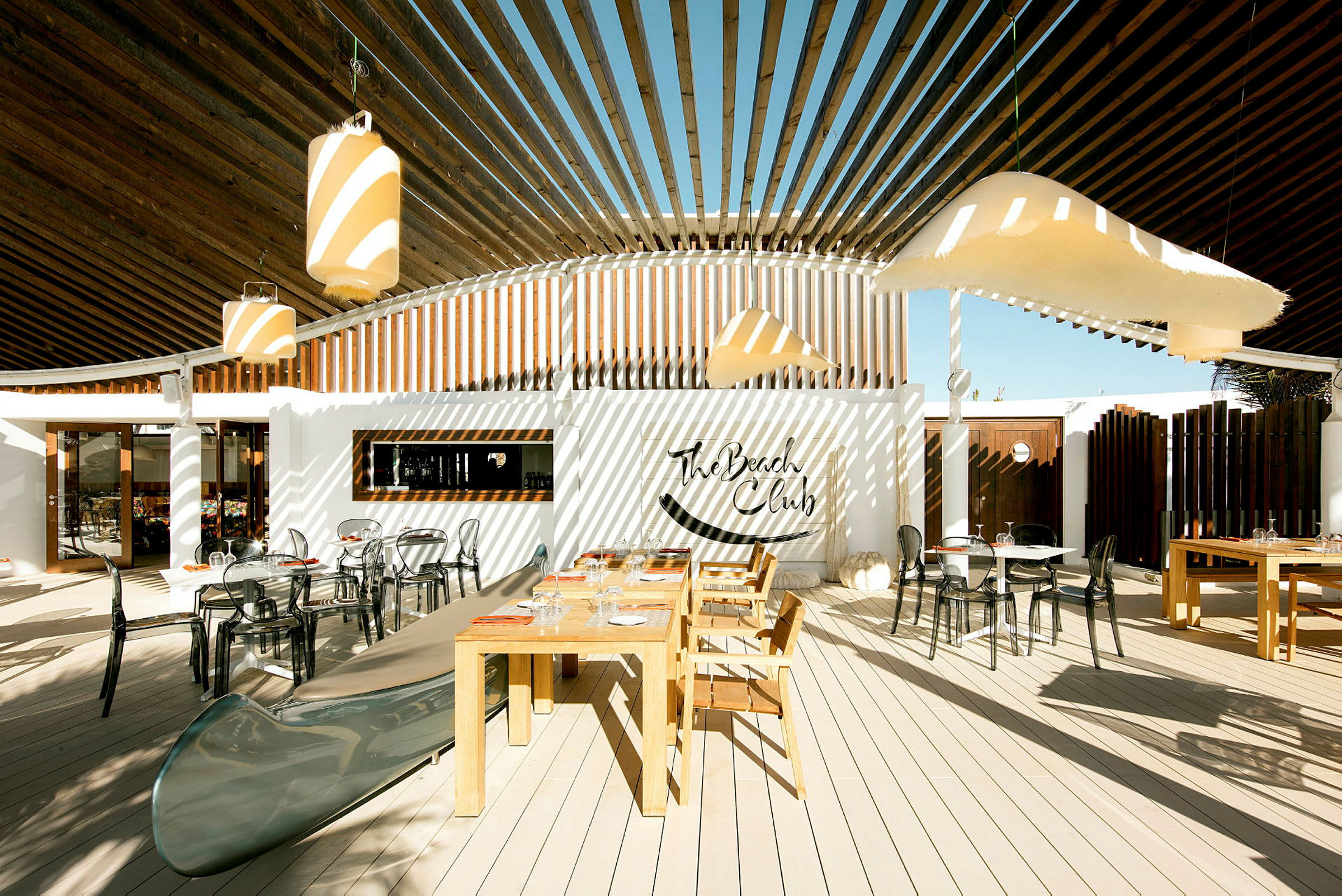 Utomhusområde med bord och stolar, samt dekoration med The Beach Club-skylt. (AI-genererad text)
