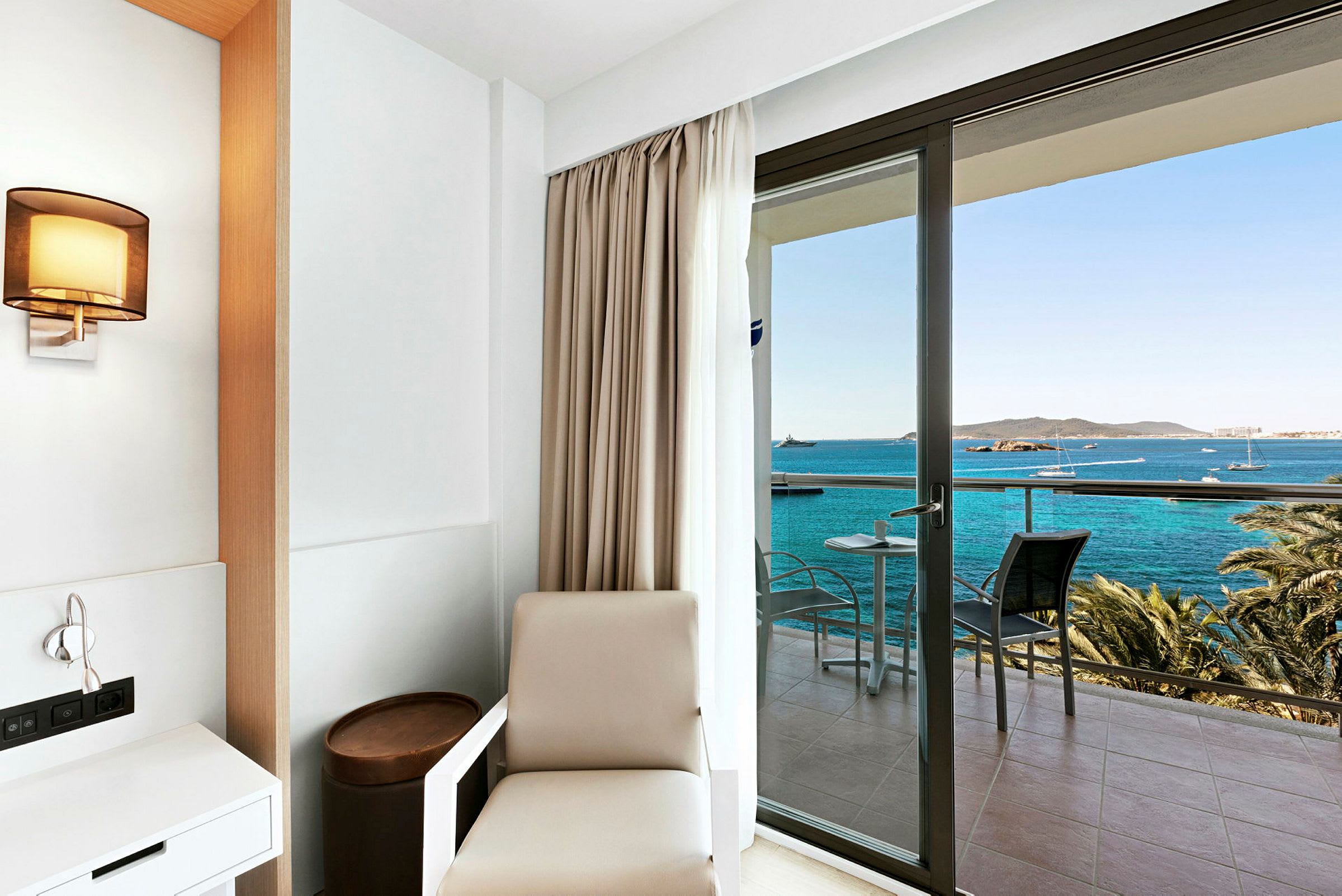 Hotellrum med minimalistisk inredning och utsikt över havet från en balkong. (AI-genererad text)