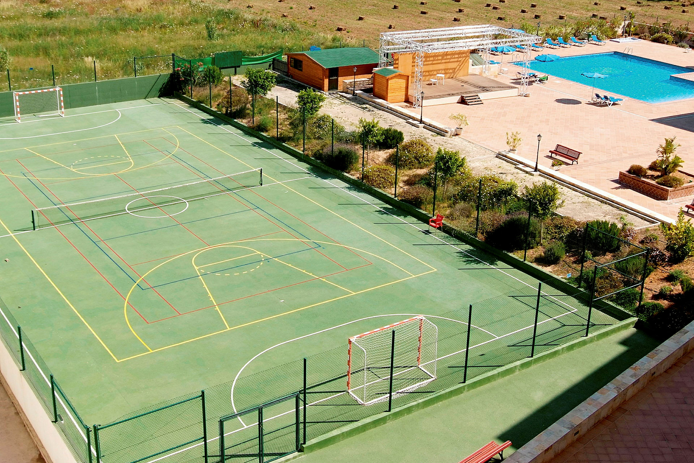 En sportplan omgiven av stängsel med flera banor samt en närliggande pool och sittområden. (AI-genererad text)