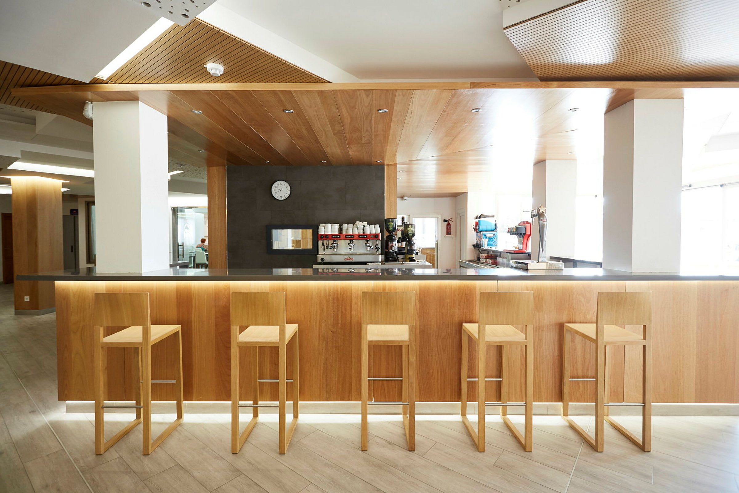 Interiörbild av en modern bar med fem trästolar framför en bardisk av trä. (AI-genererad text)