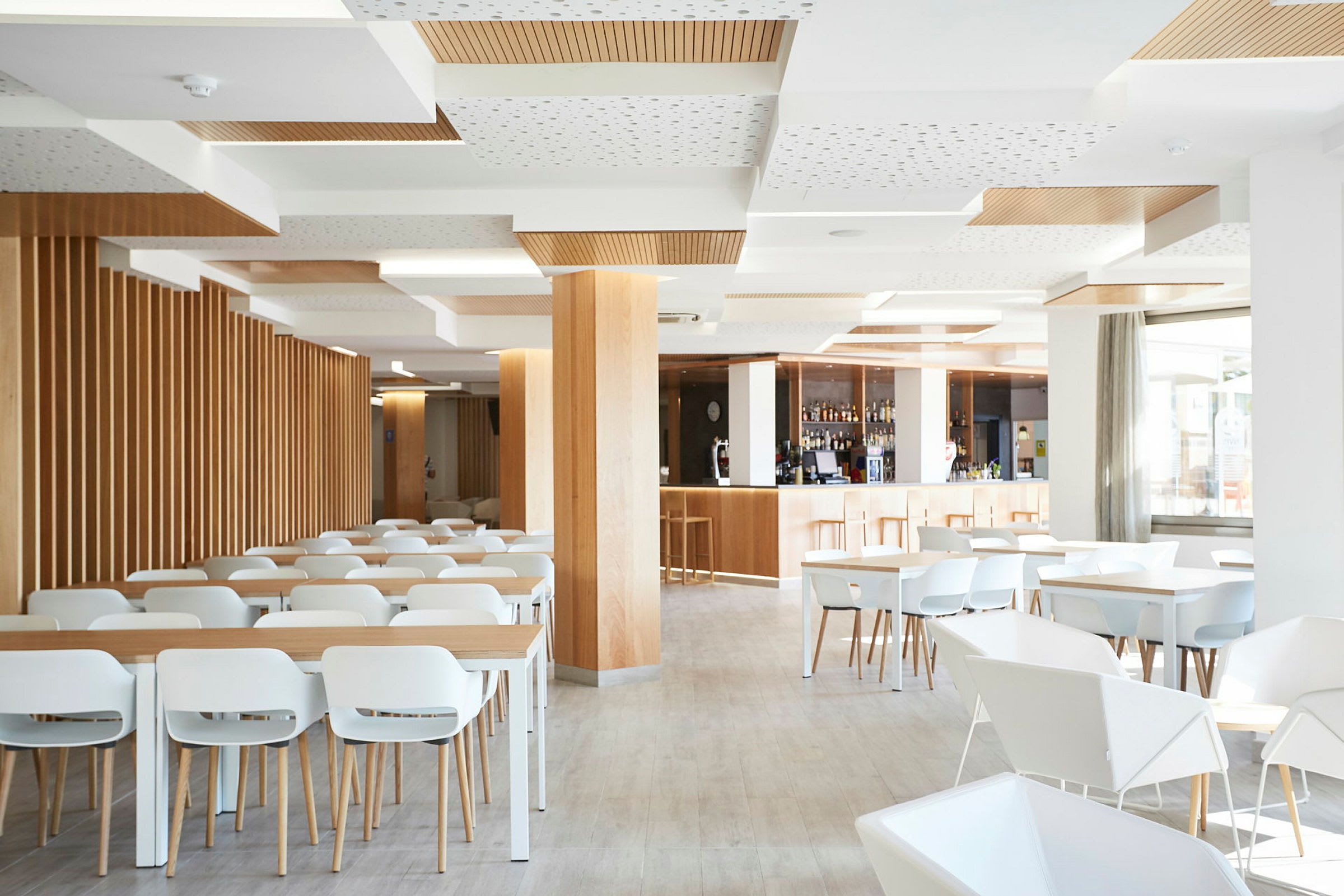En ljus och modern restaurang med vita stolar och bord, trädetaljer och en bardisk. (AI-genererad text)