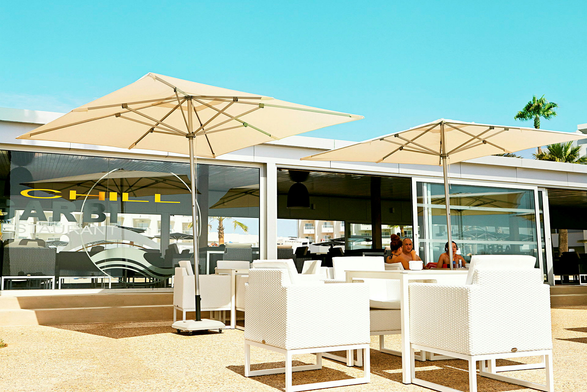 En restaurangterrass med vita möbler och stora parasoll. (AI-genererad text)
