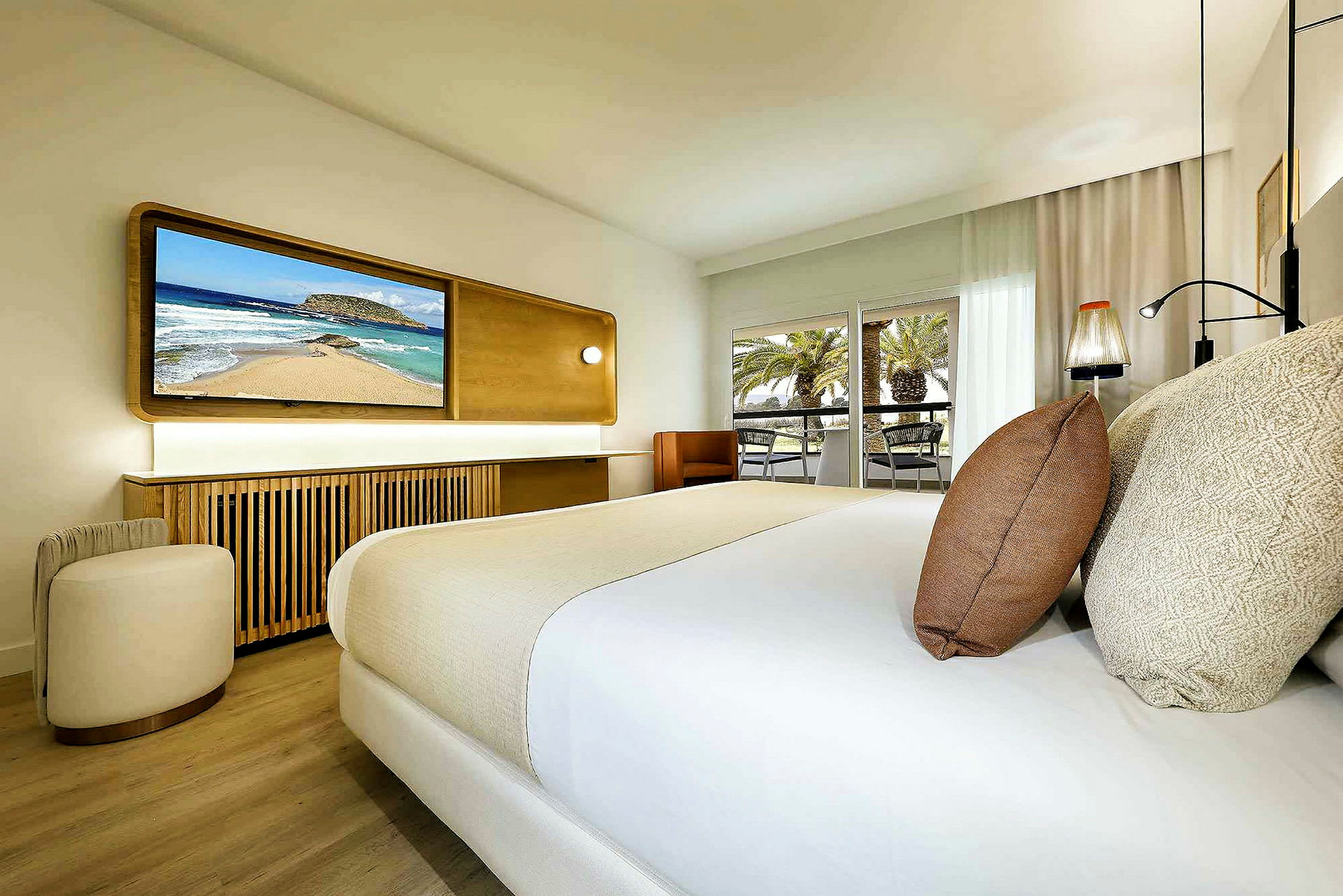 Ett modernt hotellrum med en dubbelsäng, en TV på väggen och en balkong med utsikt över palmer. (AI-genererad text)