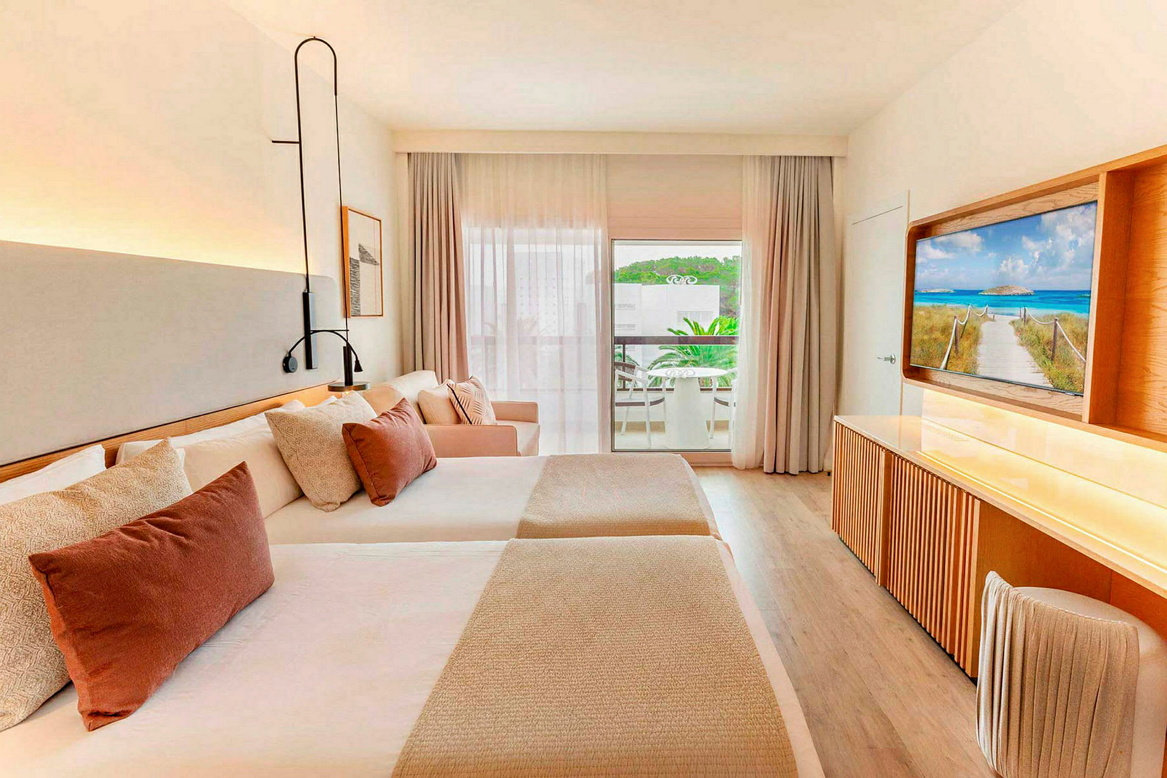 Ett hotellrum med två sängar, en soffa och en TV, samt en balkong med uteplats utanför. (AI-genererad text)
