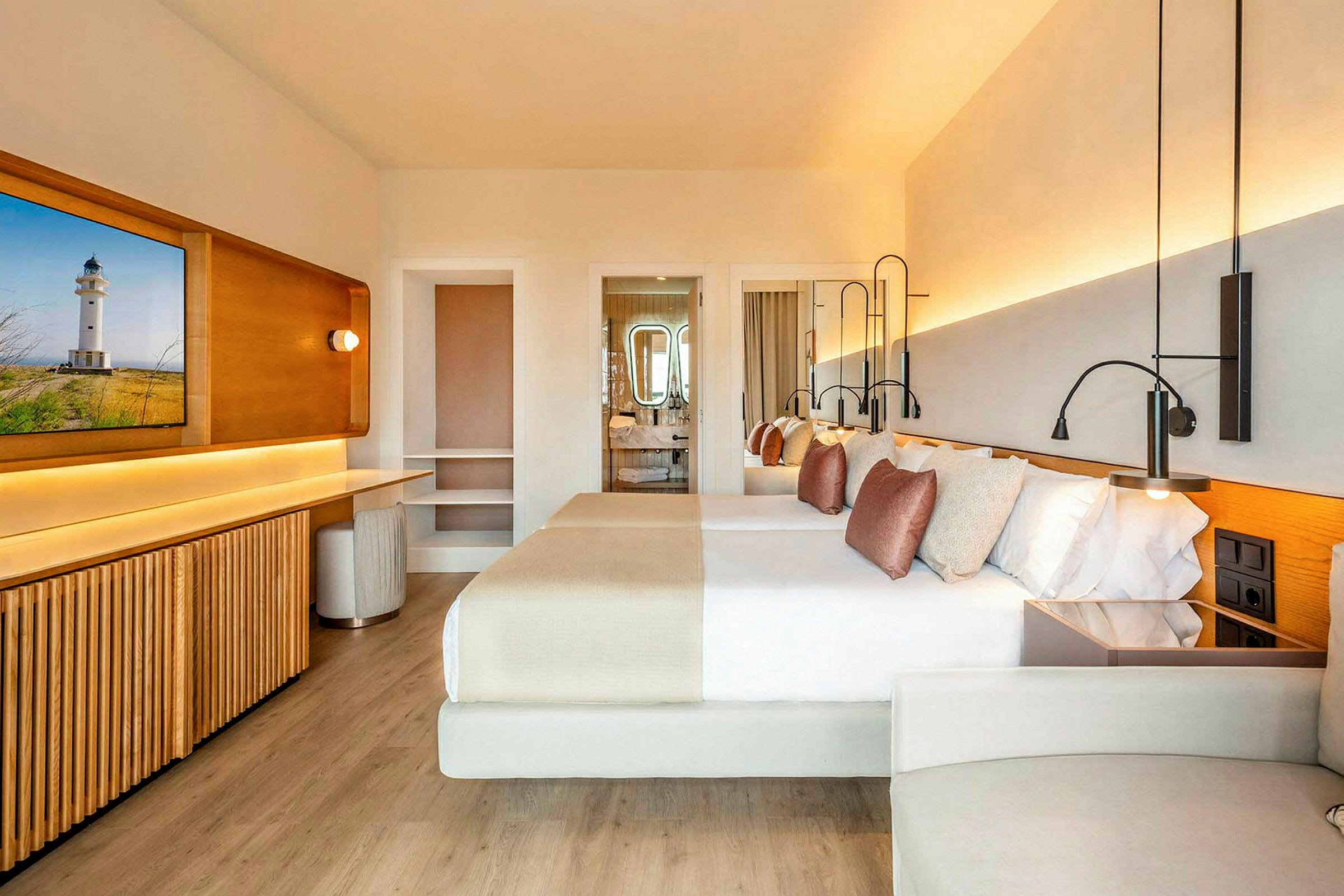 Ett modernt hotellrum med ljus inredning, två dubbelsängar med dekorativa kuddar, ett skrivbord och ett badrum i bakgrunden. (AI-genererad text)