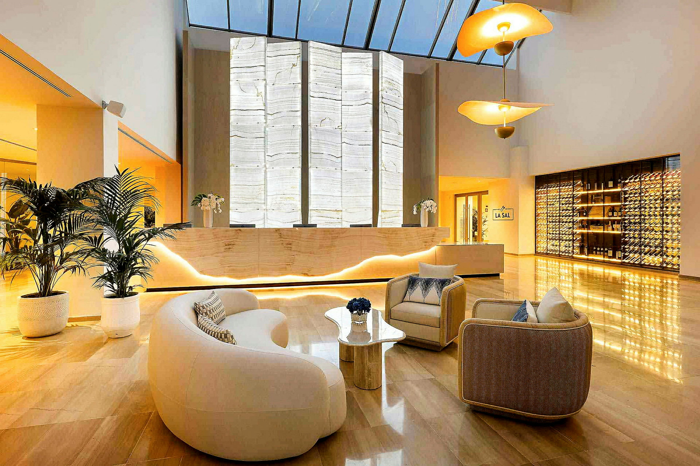 Ett modernt hotellfoajé med fåtöljer, en reception med bakgrundsbelyst vägg, och en vinförvaringsdisplay. (AI-genererad text)