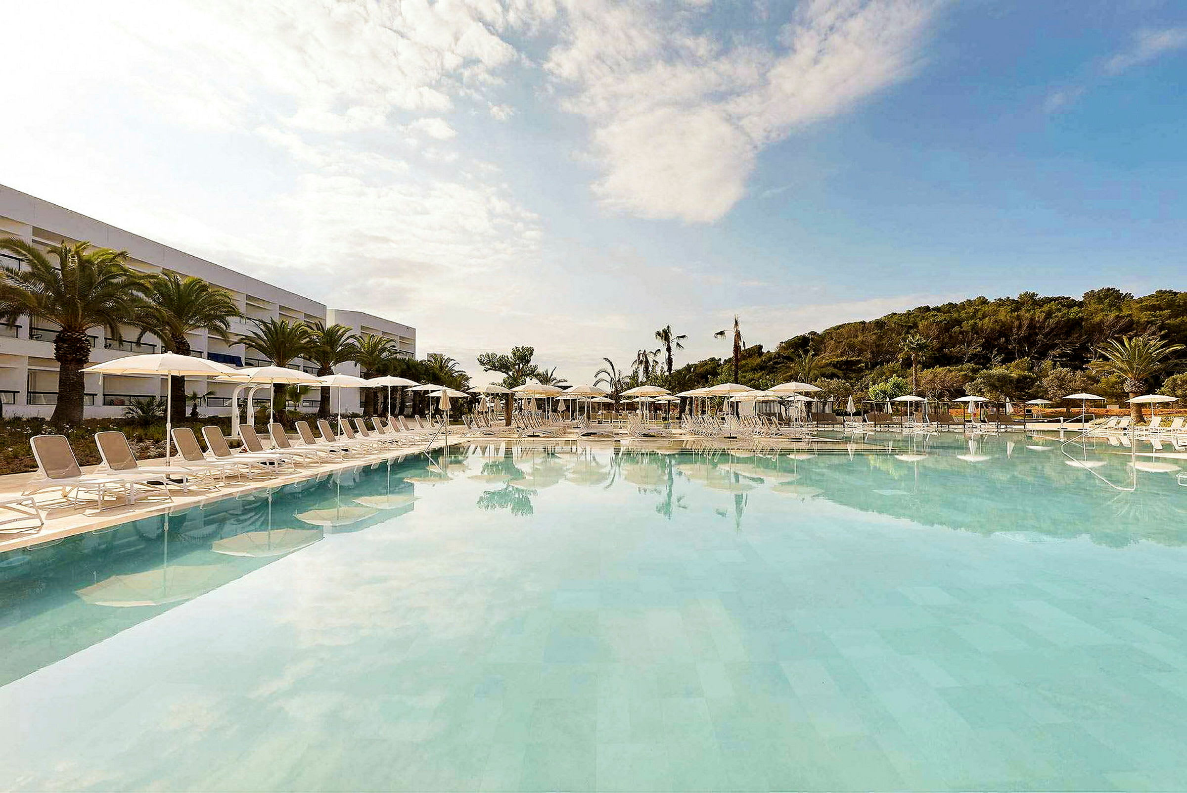 Bild av en stor pool vid ett hotell, med solstolar och parasoller på omgivande terrass. (AI-genererad text)