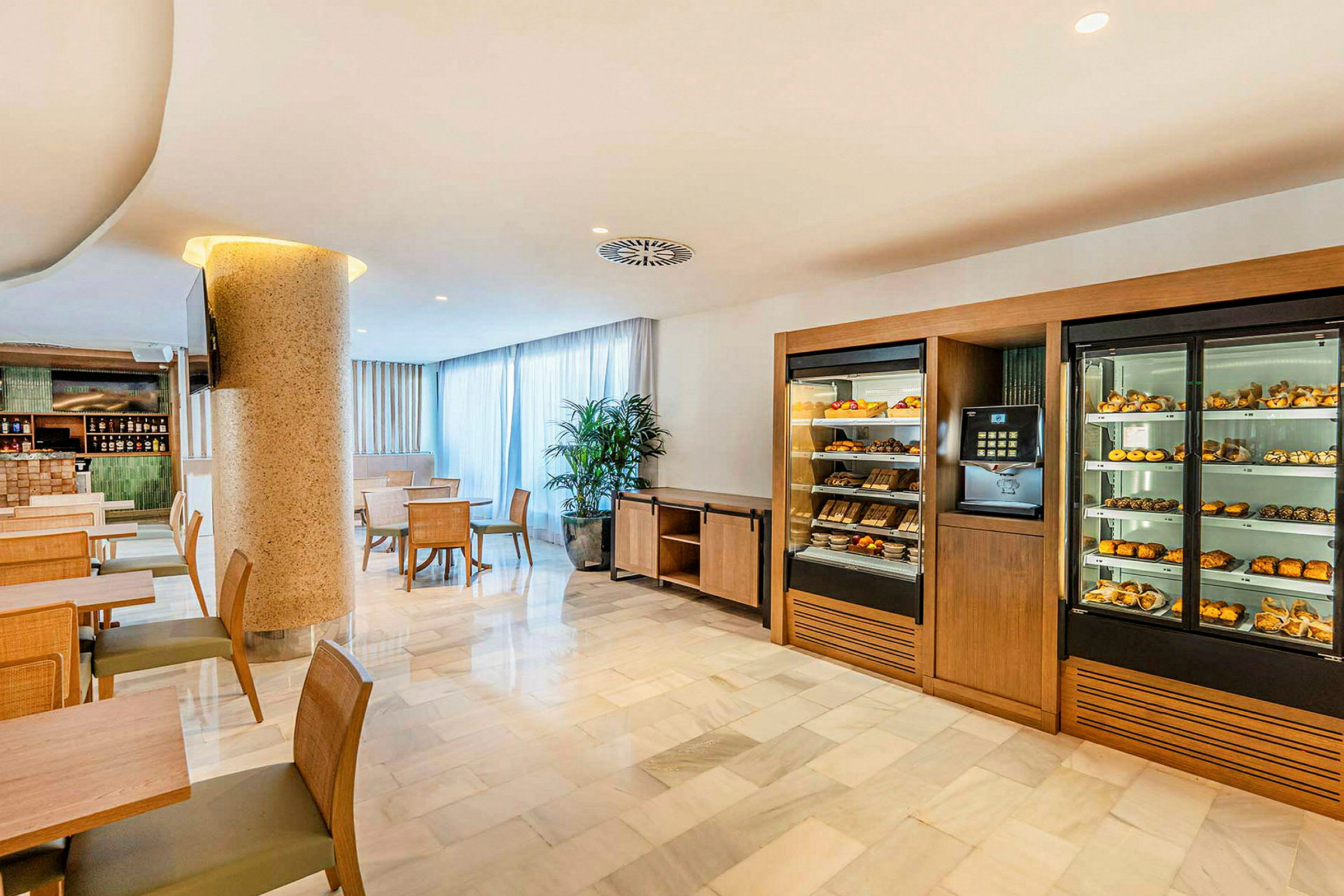 En hotellrestaurang med matbord och stolar samt skåp fyllda med bakverk och frukter. (AI-genererad text)