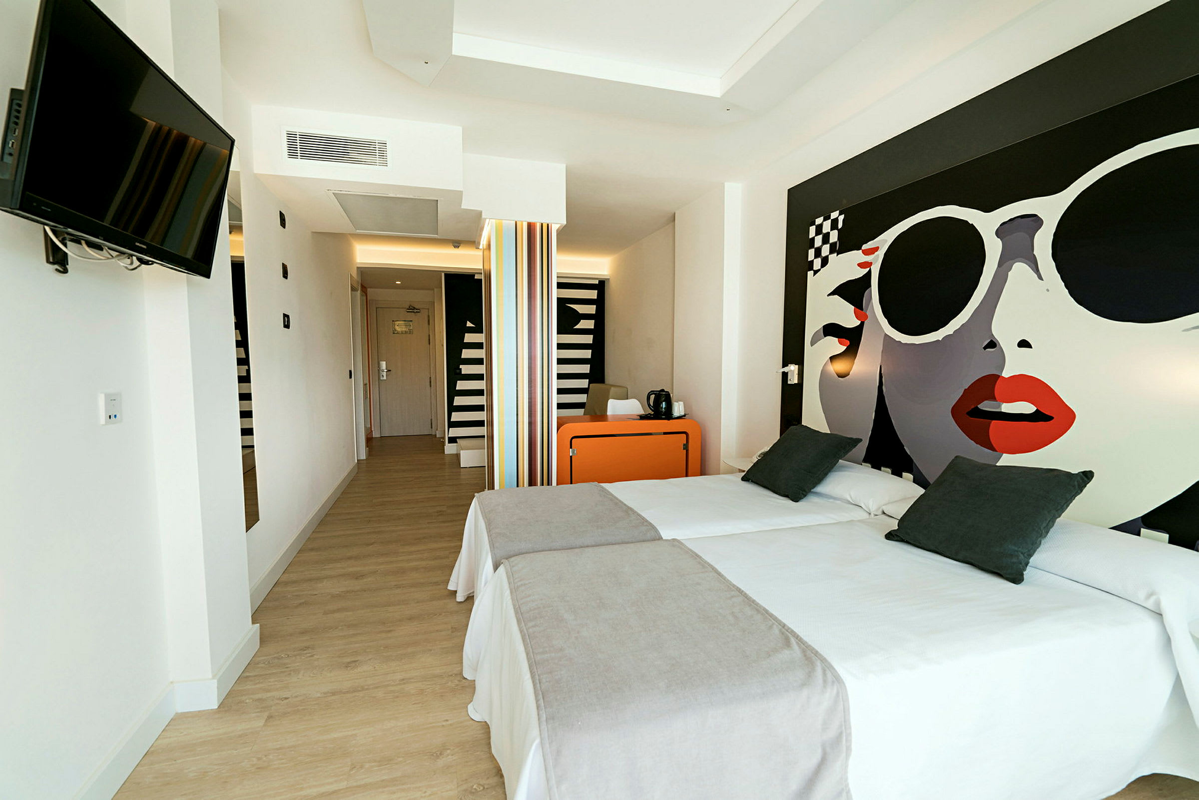 Hotellrum med två enkelsängar, ett orange skrivbord och en väggmonterad TV. (AI-genererad text)