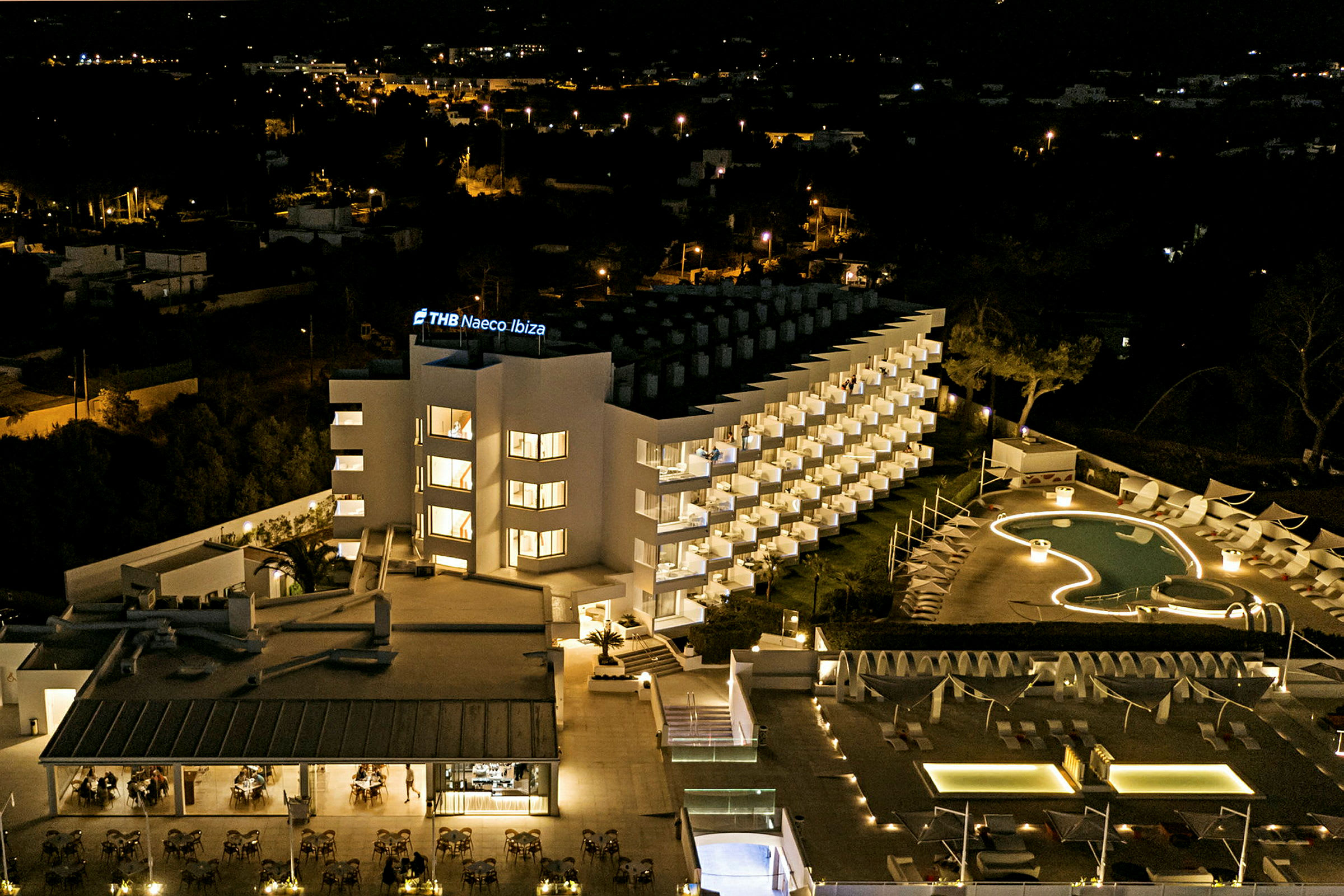 Hotell byggt i modern stil, belyst på natten med en pool framför. (AI-genererad text)